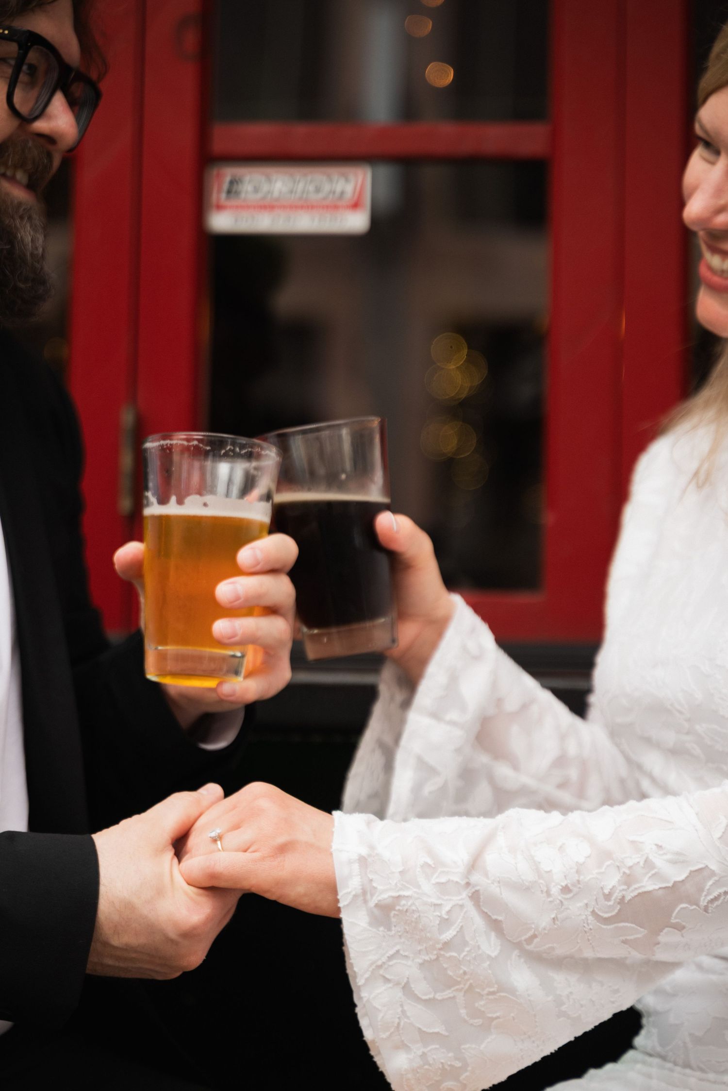 Close-up shot of hands holding glasses of golden beer in a dimly lit setting.