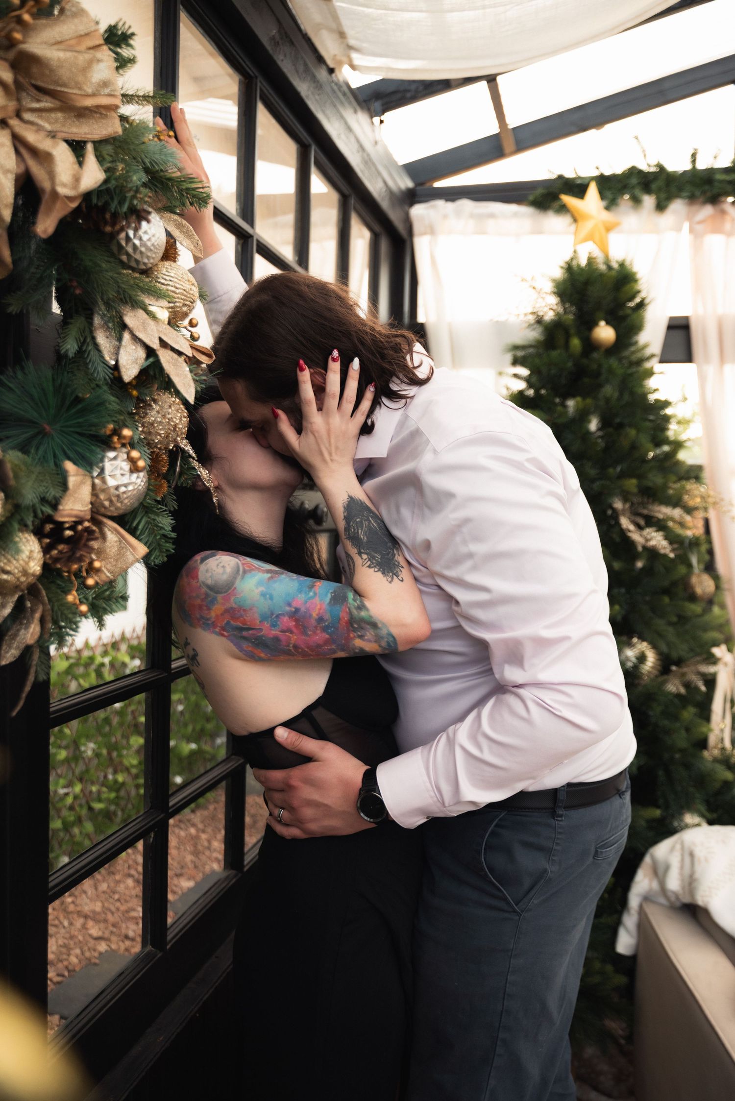 A romantic couple embraces in a cozy setting decorated with holiday greenery and twinkling lights.