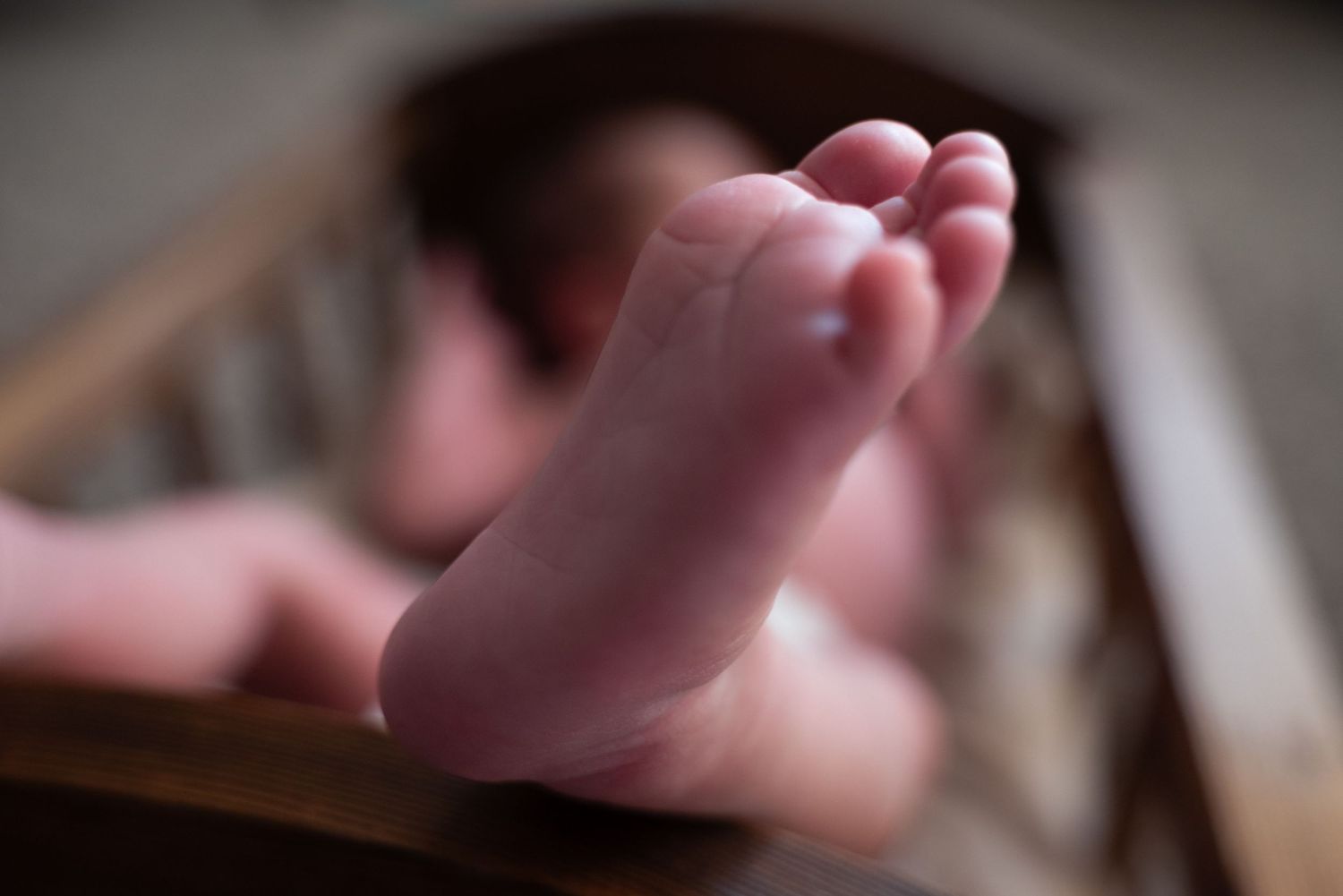 A close-up macro photograph shows a newborn baby's tiny fingers grasping against a soft, blurred background.