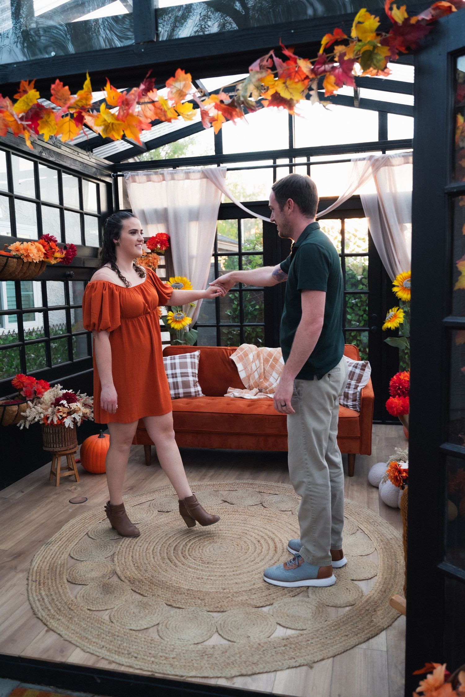 A couple dances together in a fall-decorated gazebo with pumpkins and autumn leaves strung overhead.
