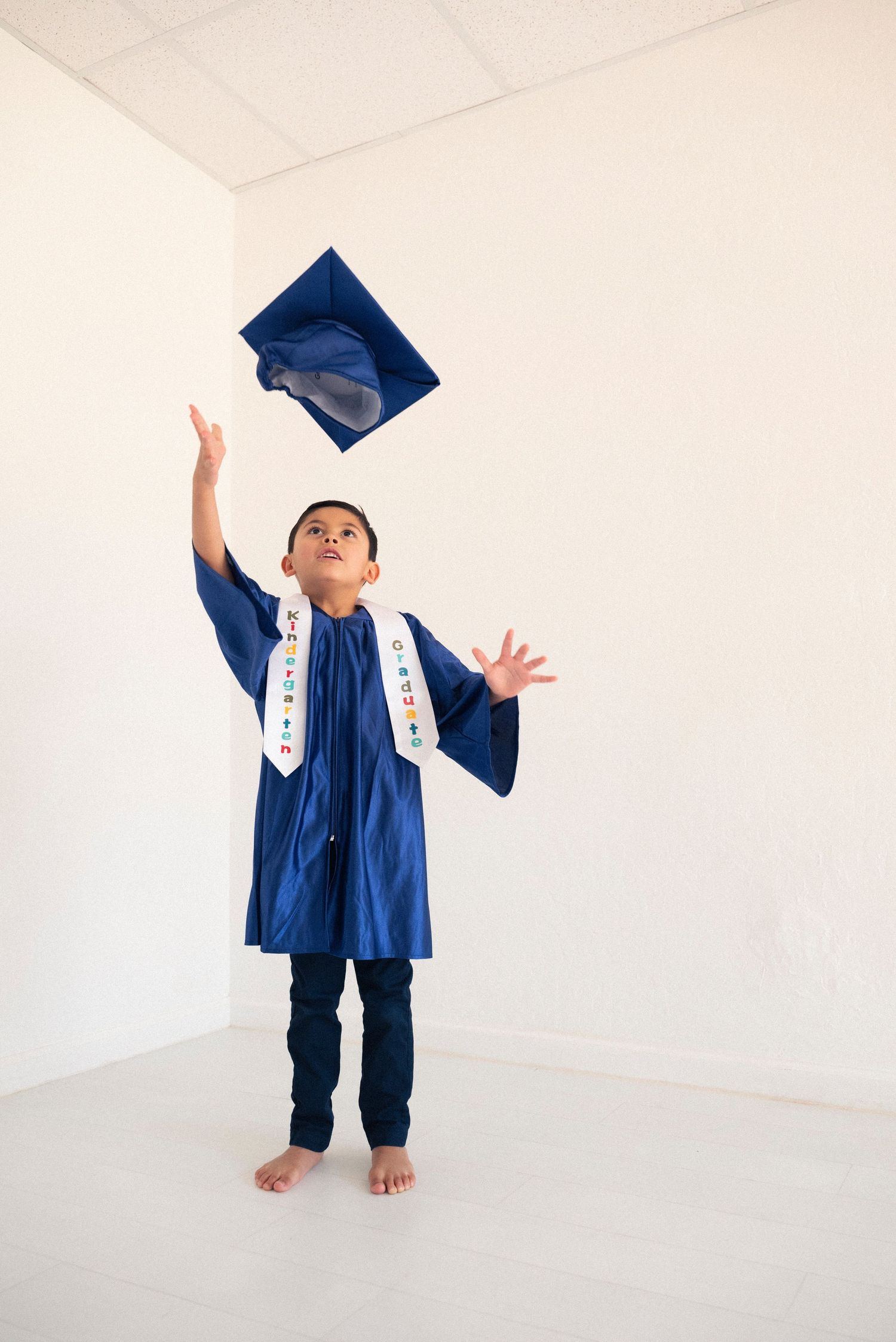 A graduate in a blue cap and gown tosses their mortarboard cap in the air during a celebratory photoshoot sequence.