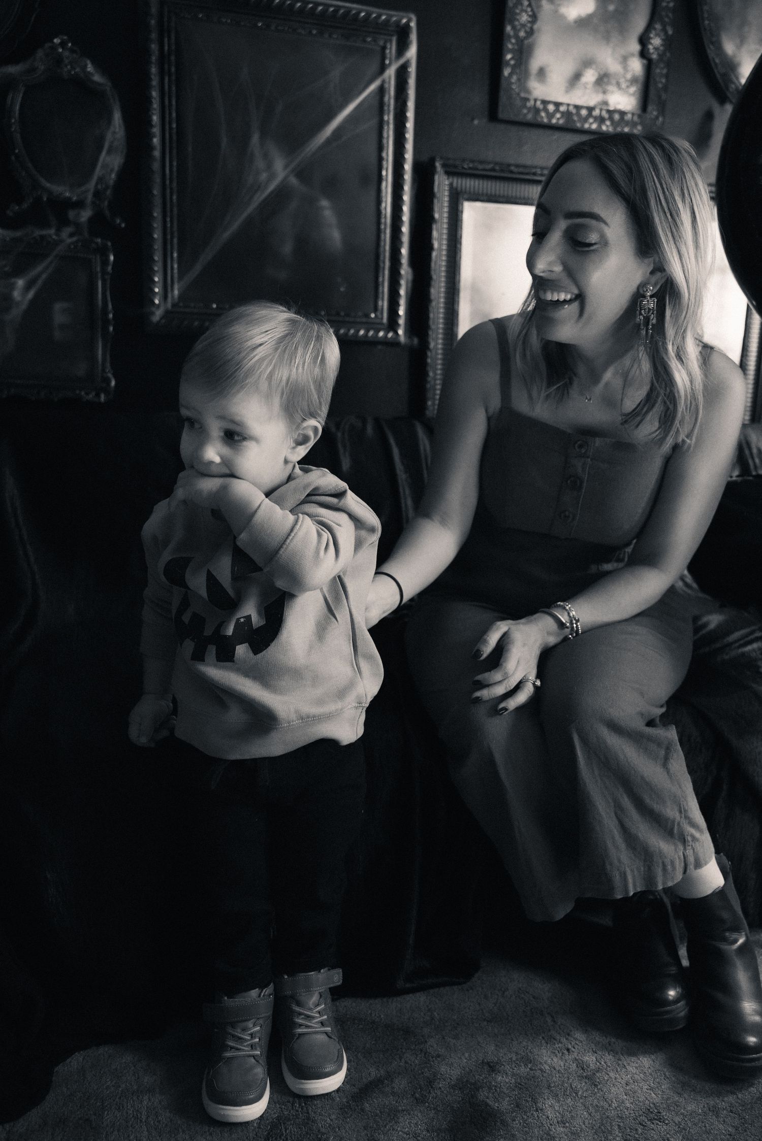 A candid black and white moment showing a toddler and adult sitting together in a room with framed artwork on the walls.
