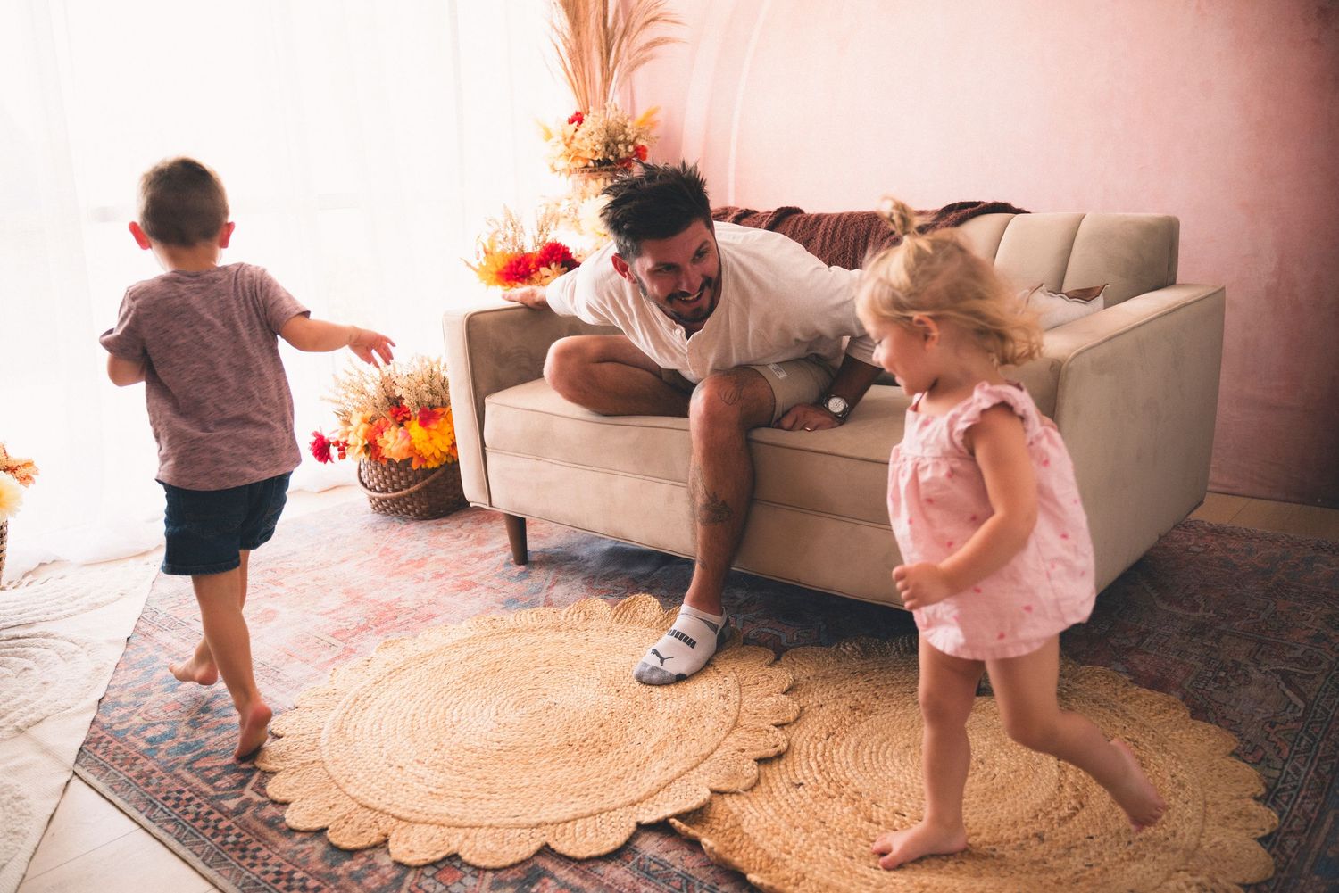 Children dancing on a carpet in a room with colorful toys and activity mats scattered around.