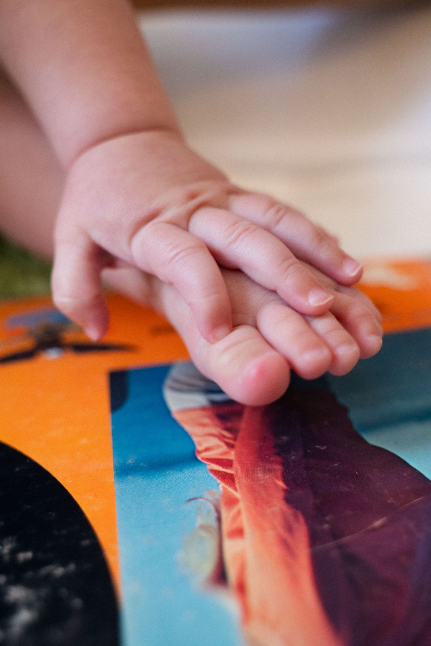 Close-up sequence showing a baby's hand touching and exploring colorful paper surfaces in warm lighting.
