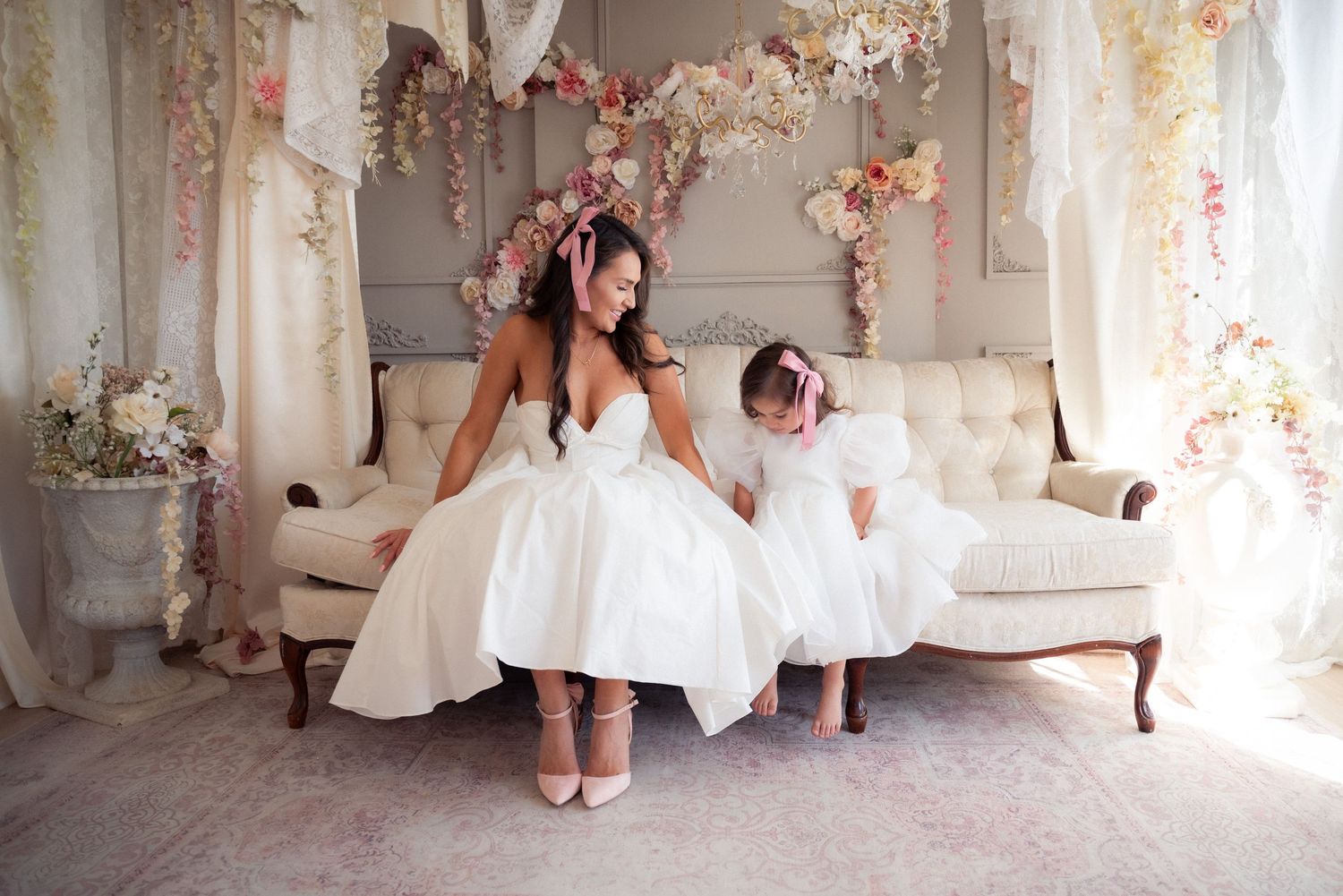 A wedding dress detail shot with pink floral decorations and elegant white decor in the background.