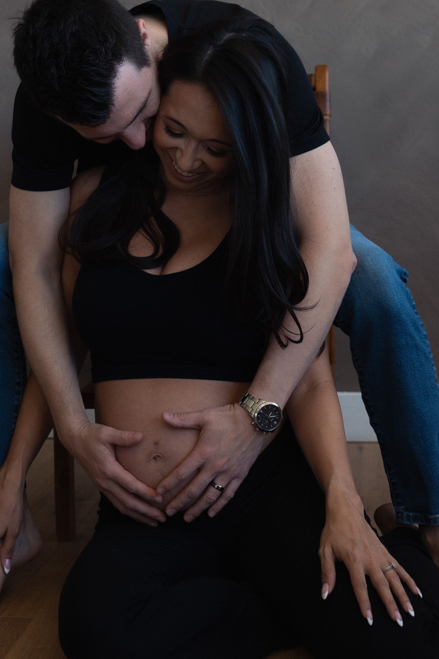 A couple shares a tender moment, with a man kissing a smiling pregnant woman's head while both cradle her baby bump.