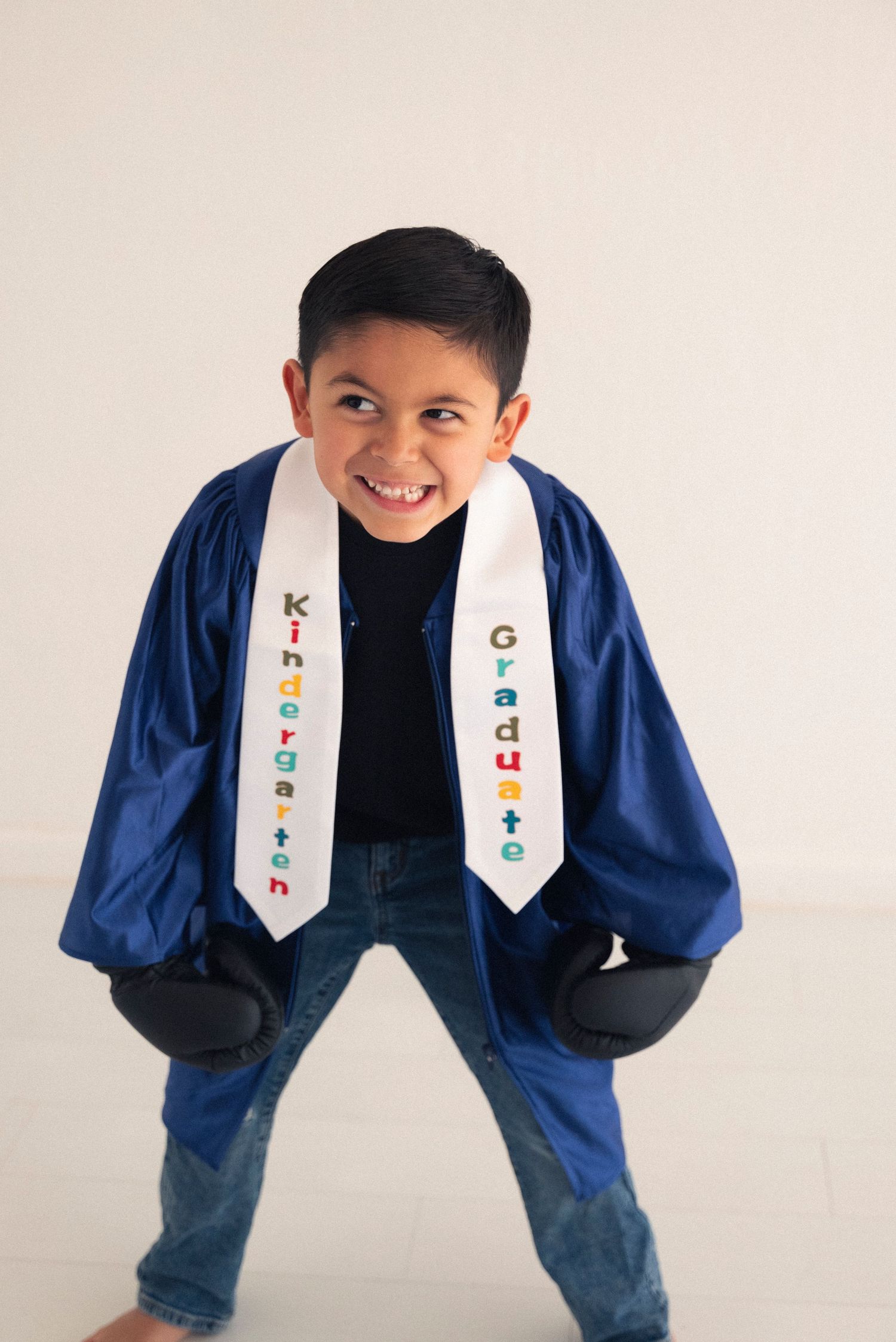 A joyful figure in a blue graduation gown and decorative white stole shows four different playful poses against a white wall.