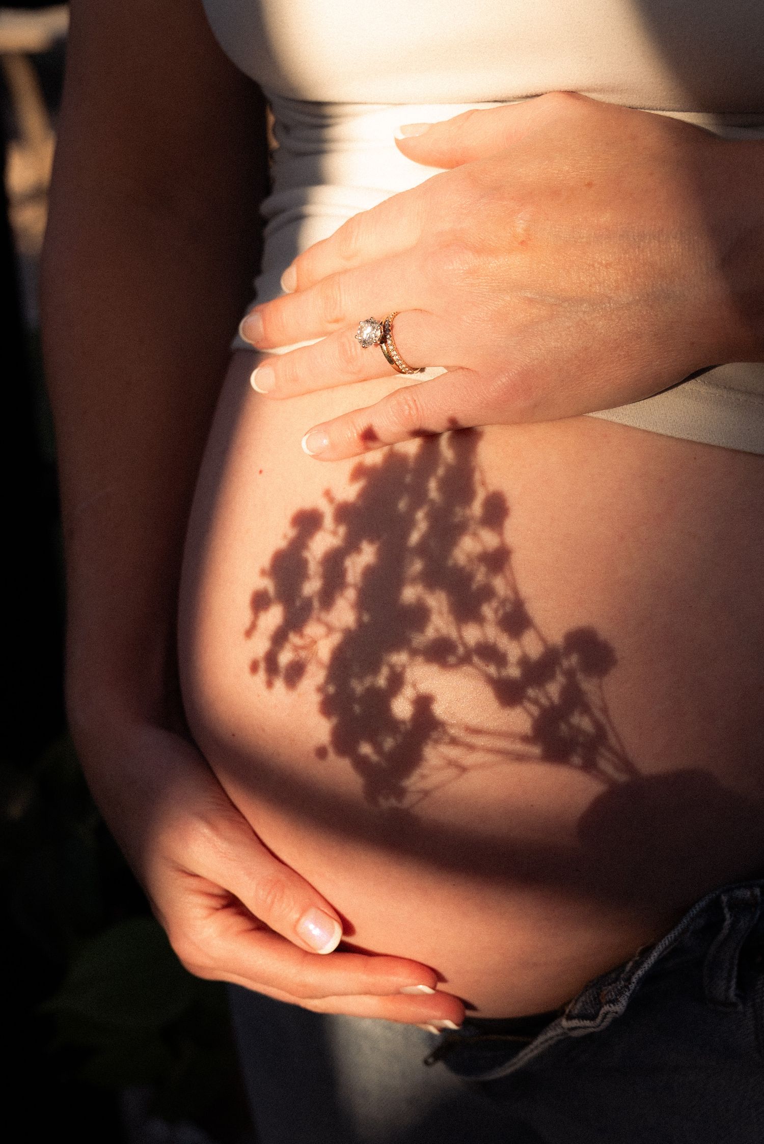 Artistic maternity photo series showing shadows of tree branches cast across a pregnant belly in warm lighting.