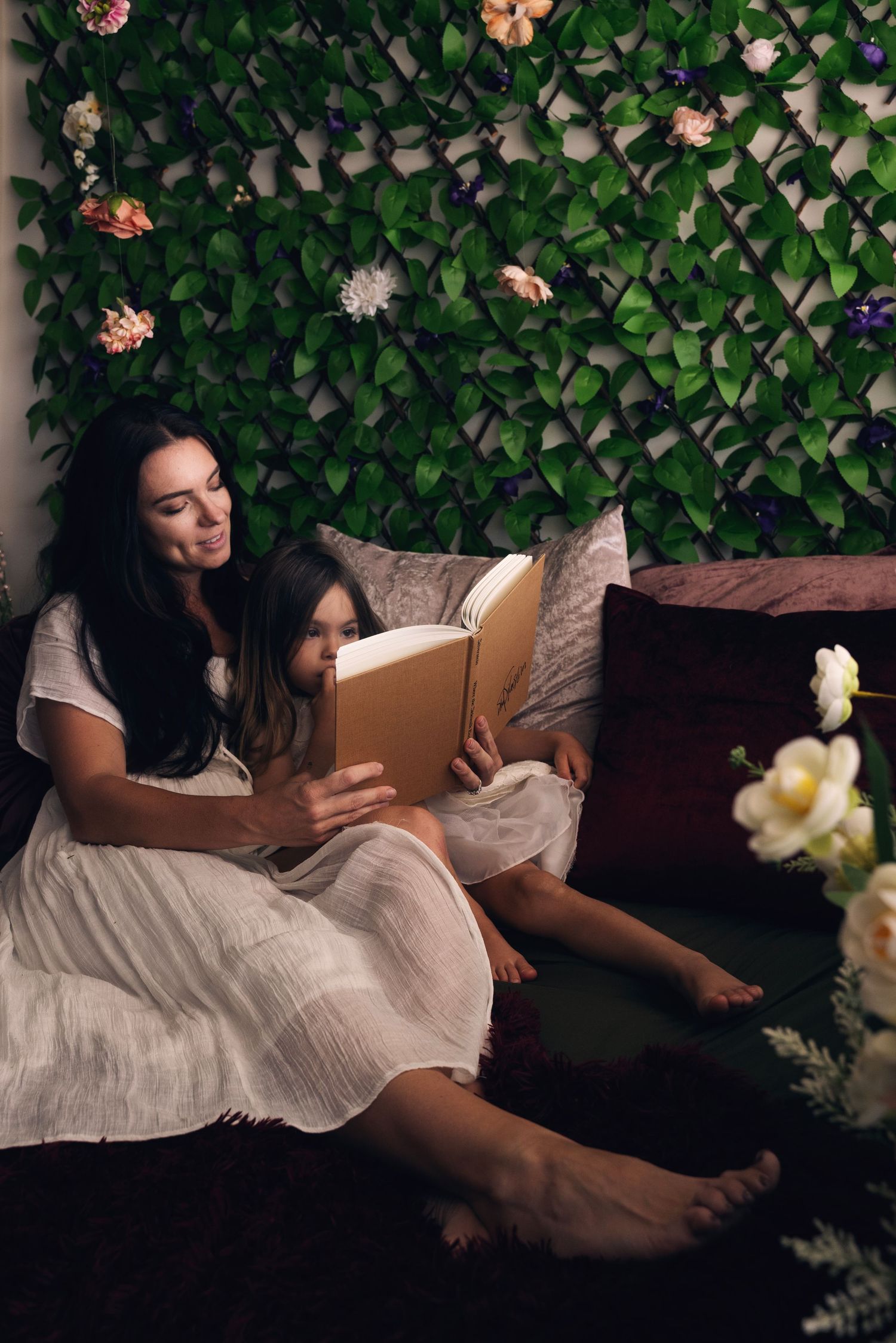 A peaceful reading moment on a dark couch against a leafy green backdrop with delicate flowers and soft lighting.