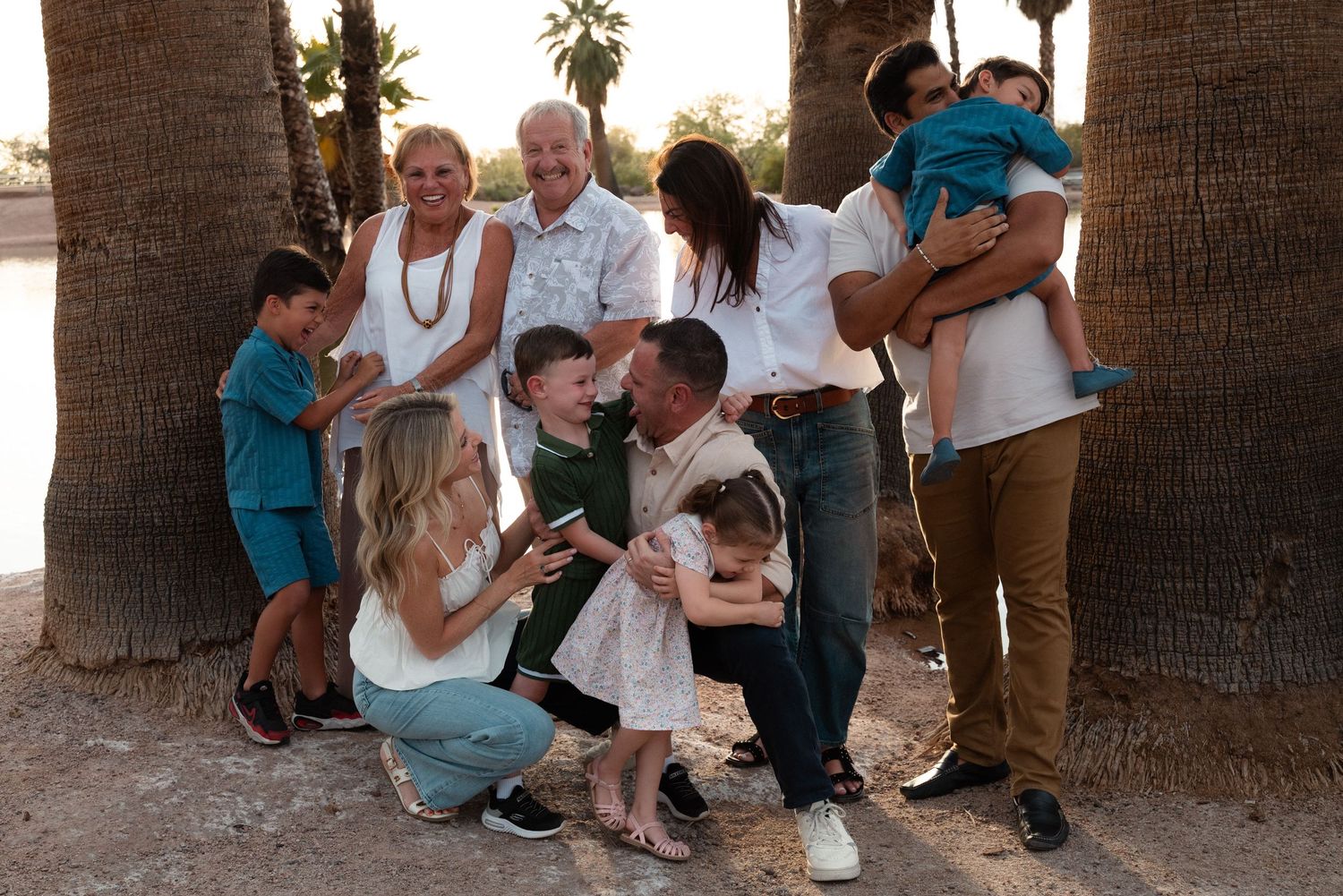 Multi-generational family portrait outdoors among palm trees, sharing joyful moments together in coordinated white and teal outfits.