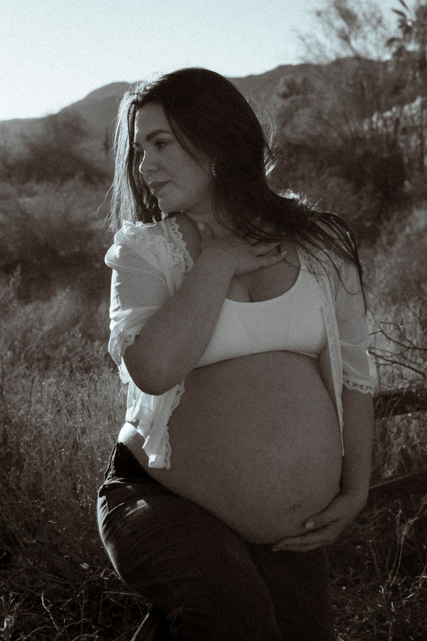 A black and white portrait of a pregnant woman in a desert setting at sunset.