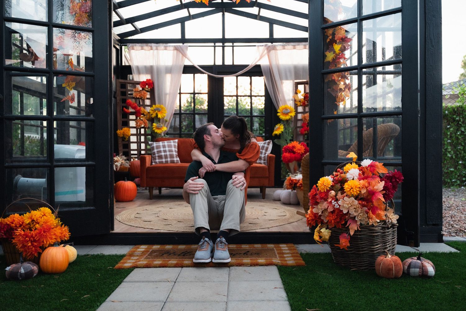 Glass greenhouse decorated with vibrant fall pumpkins and orange floral arrangements creating an autumn atmosphere.