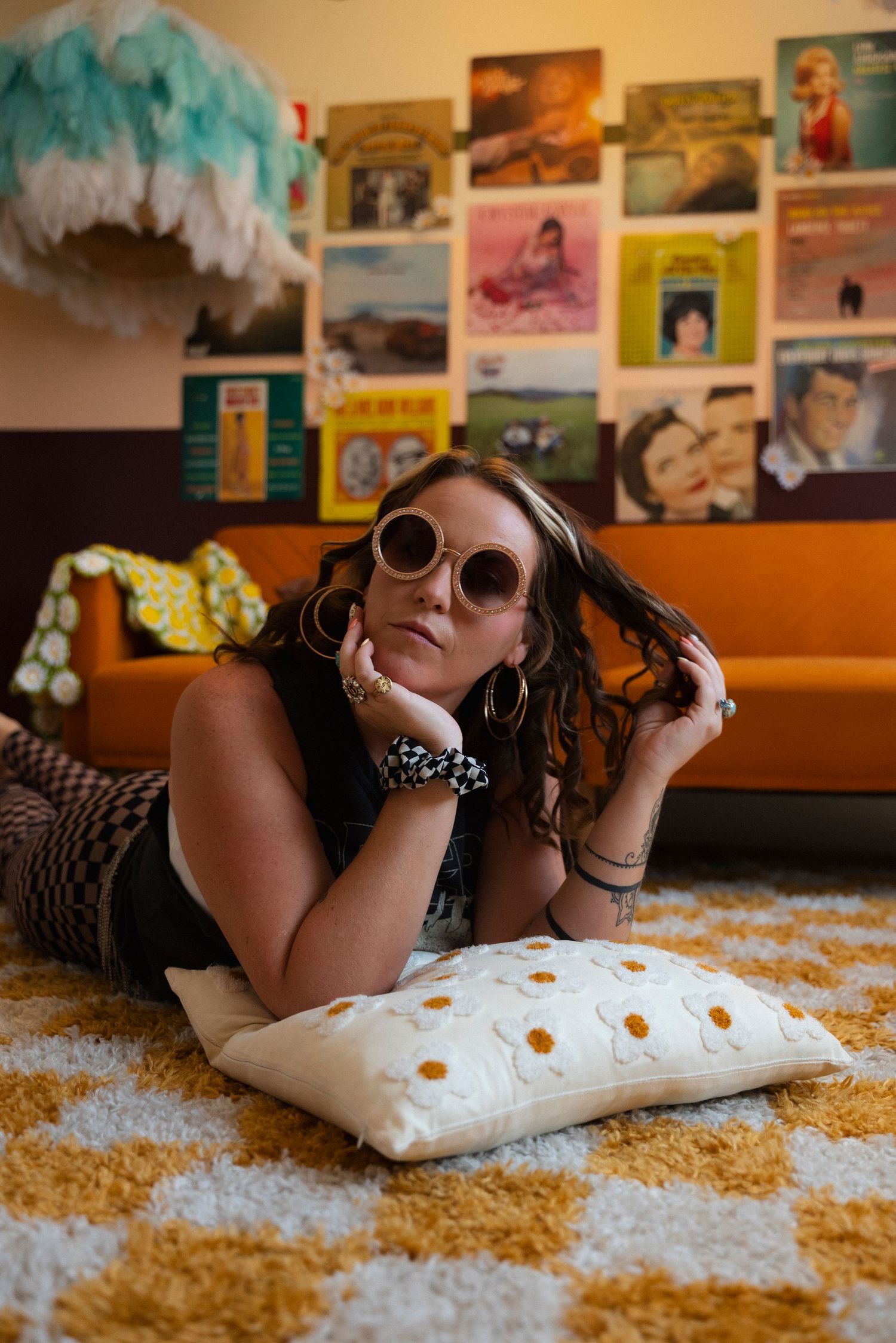 Person lying on yellow carpet with white pillow wearing sunglasses in room with photos on wall.