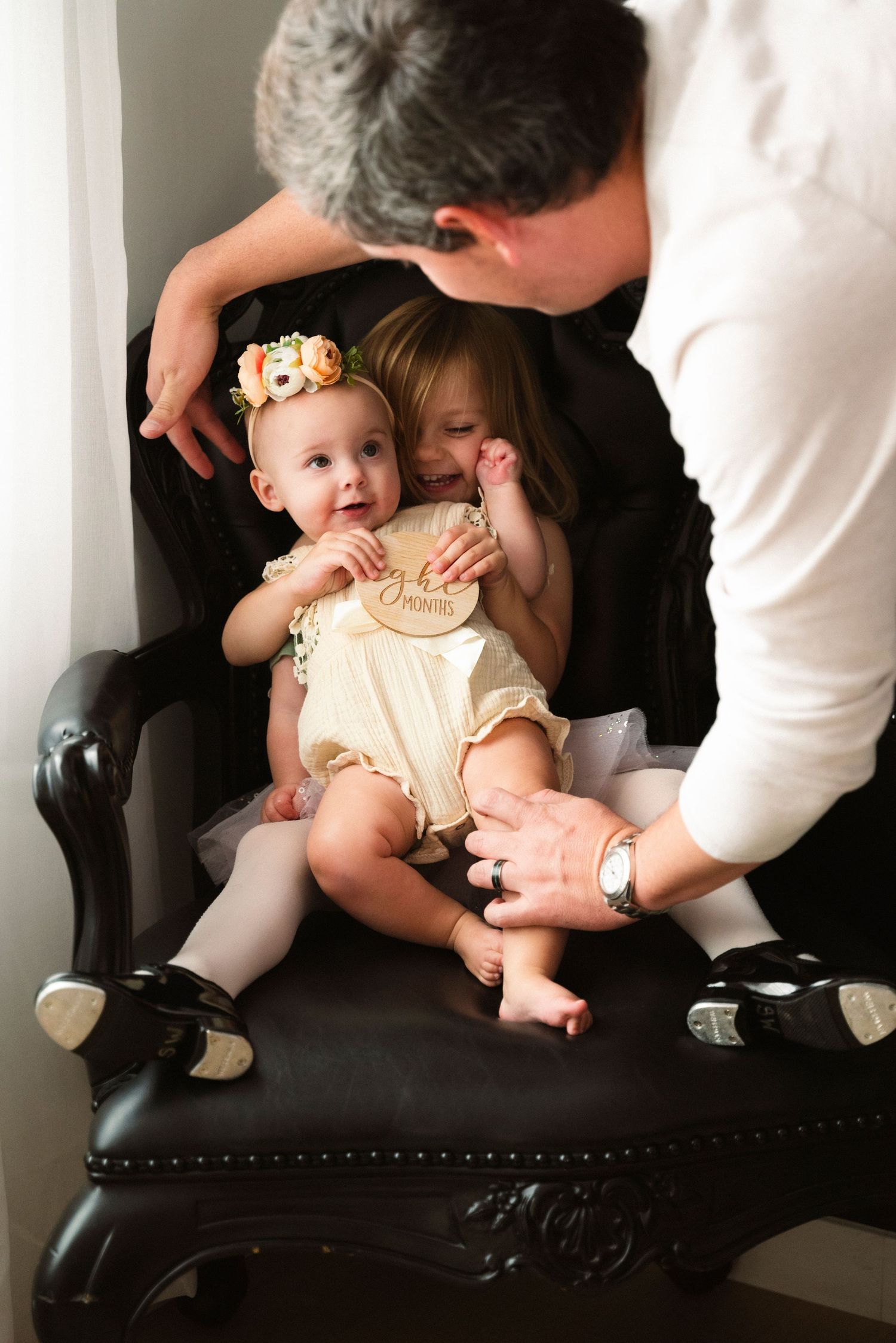 Sequence of photos showing a baby in cream-colored outfit being photographed on black leather furniture during a photo session.