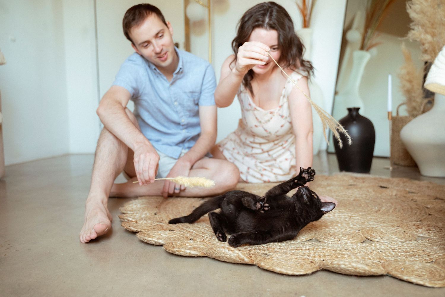 A couple plays with their black cat on a woven jute rug in their bright living room.