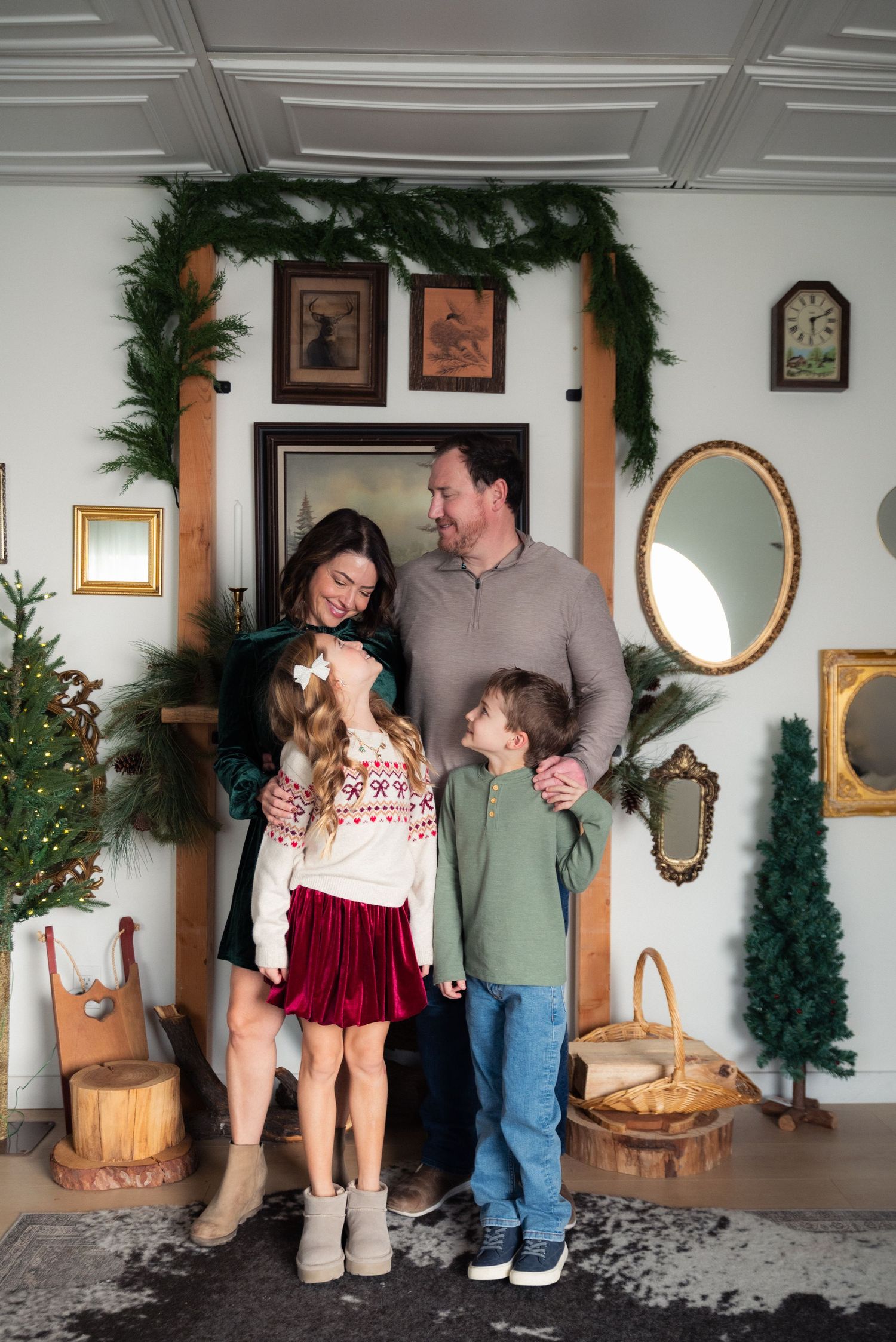 Family of four posing together in a festively decorated room with Christmas garland and holiday decor.