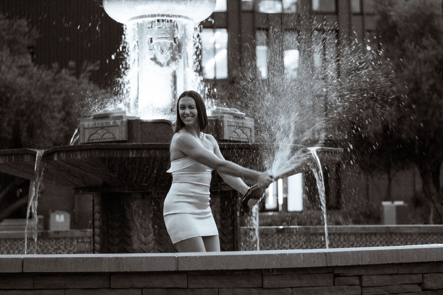People playing and splashing in a public fountain on a hot summer day at a city park.