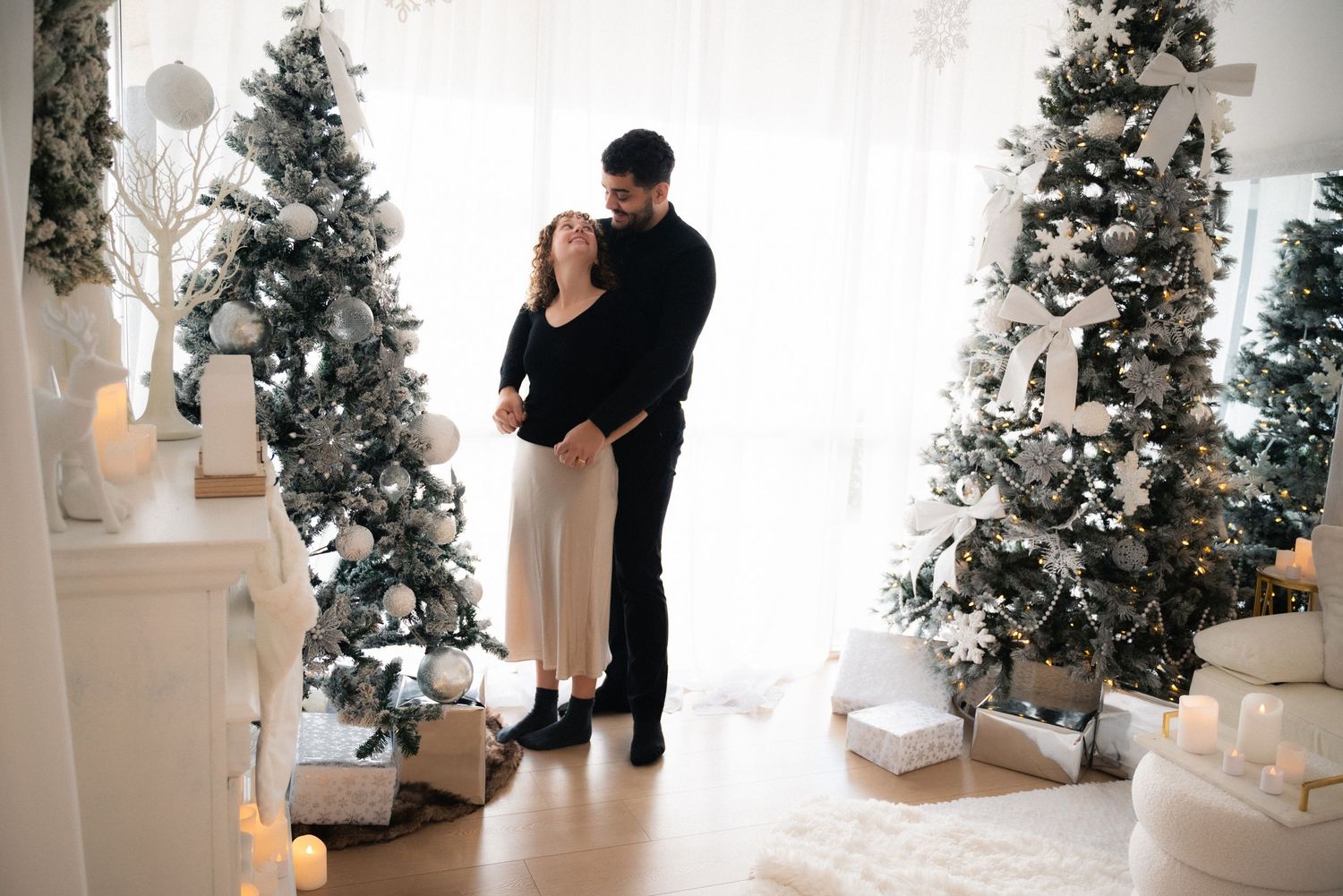 Multiple white Christmas trees with lights create festive holiday display in bright minimalist interior.