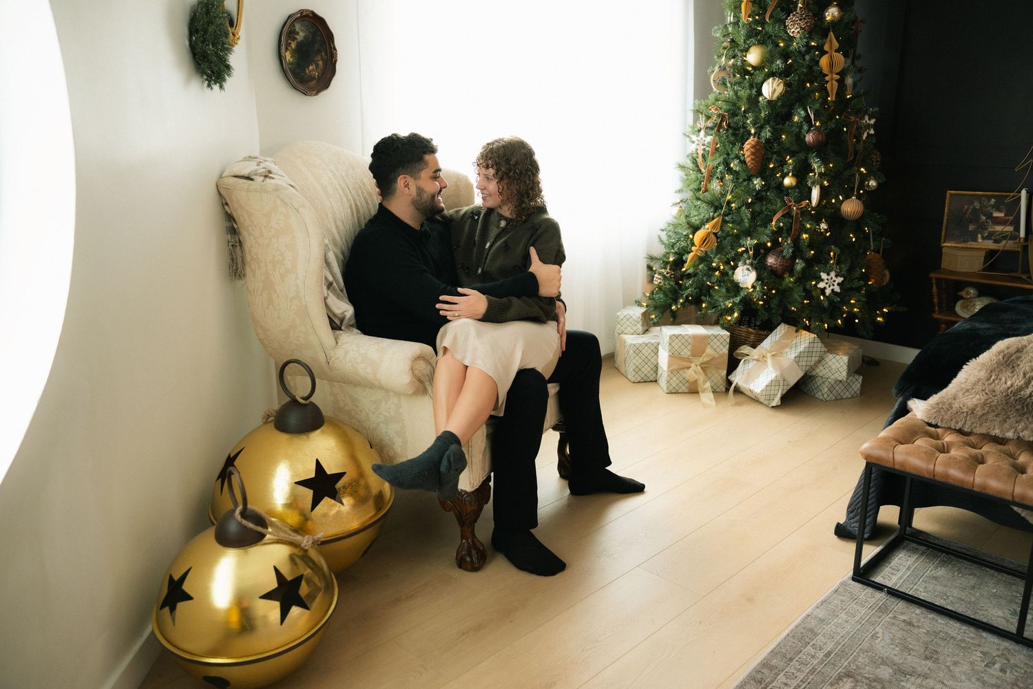 A romantic Christmas photoshoot scene with a decorated tree, candles, and couple sitting together in a cozy room.