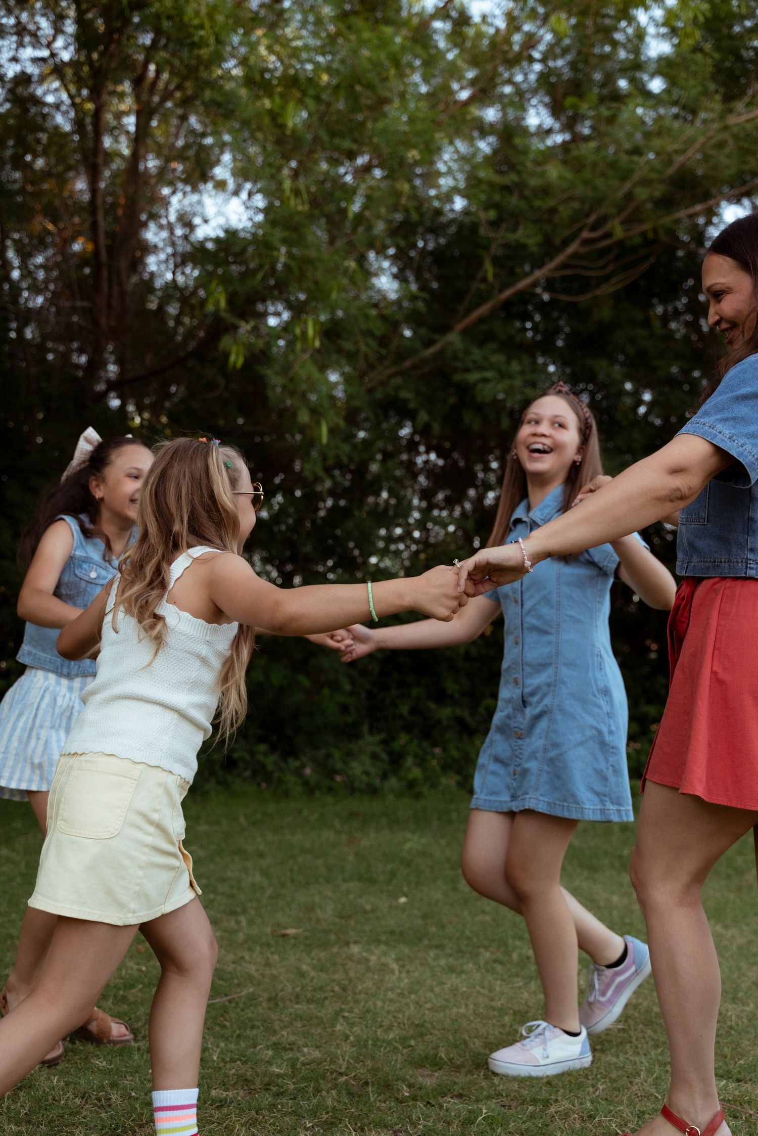 A group of friends holding hands in a circle and dancing together outdoors on a sunny day in casual summer outfits.