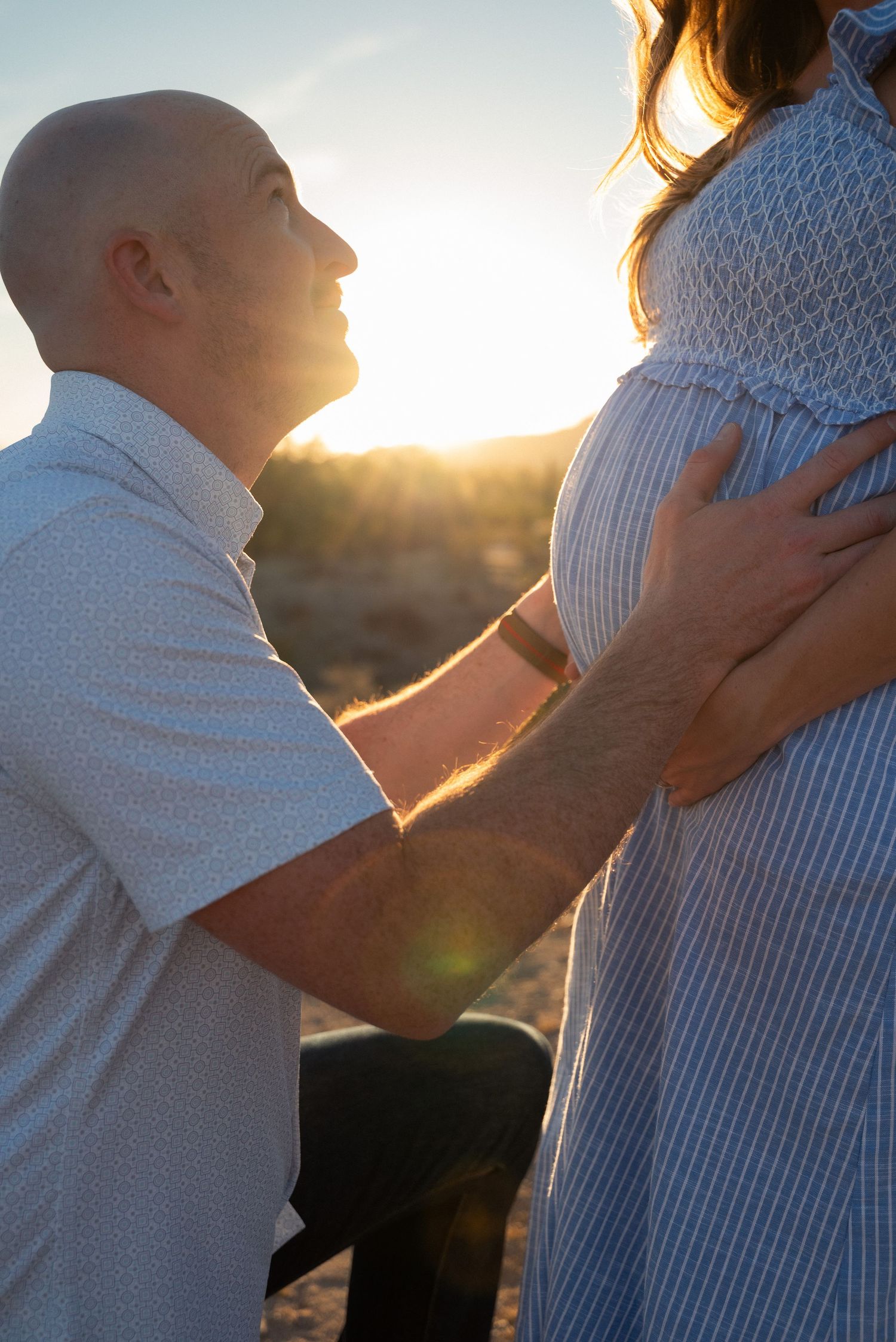 A tender moment between an expectant couple silhouetted against a golden sunset as they embrace the pregnant belly.