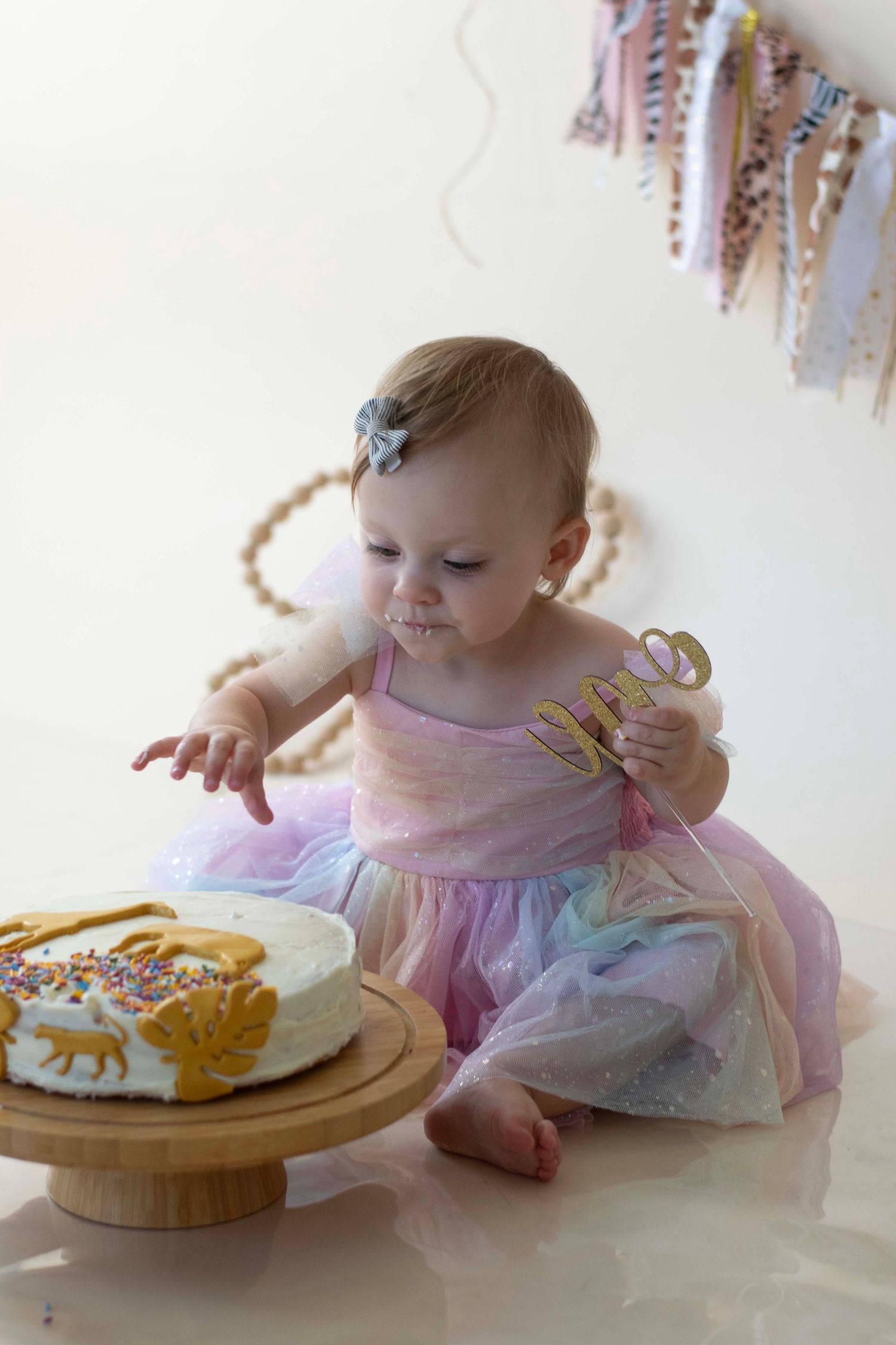 A small child in a pink and purple tulle dress reaching excitedly for cake during a celebratory photoshoot.