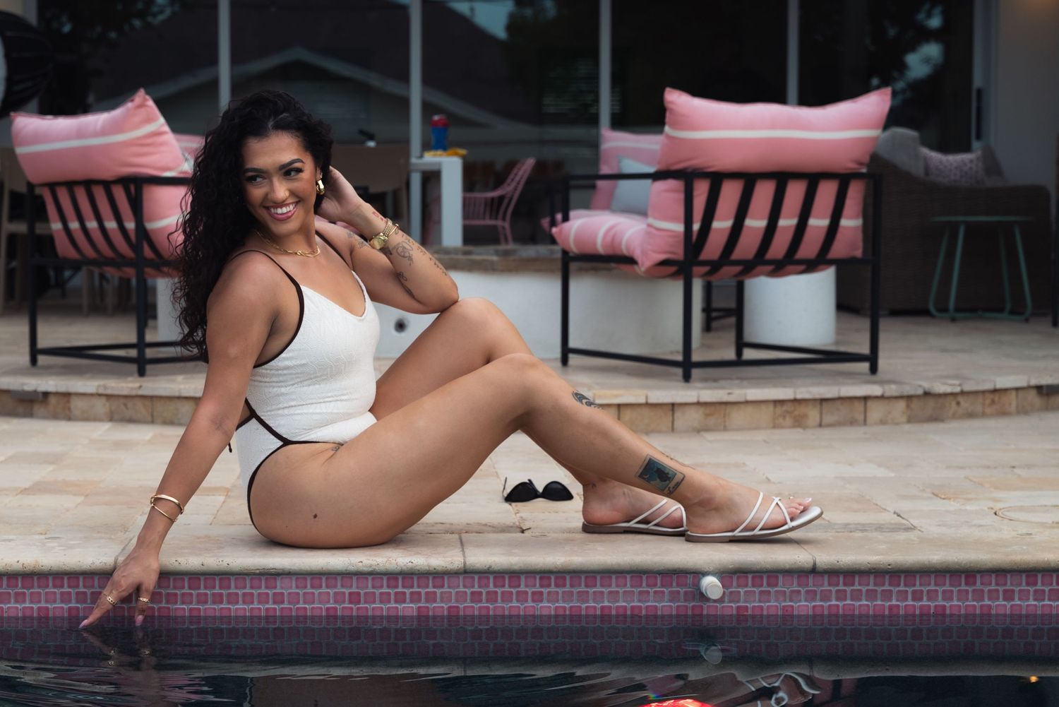 Woman in white swimsuit relaxing by pool edge on sunny summer day.