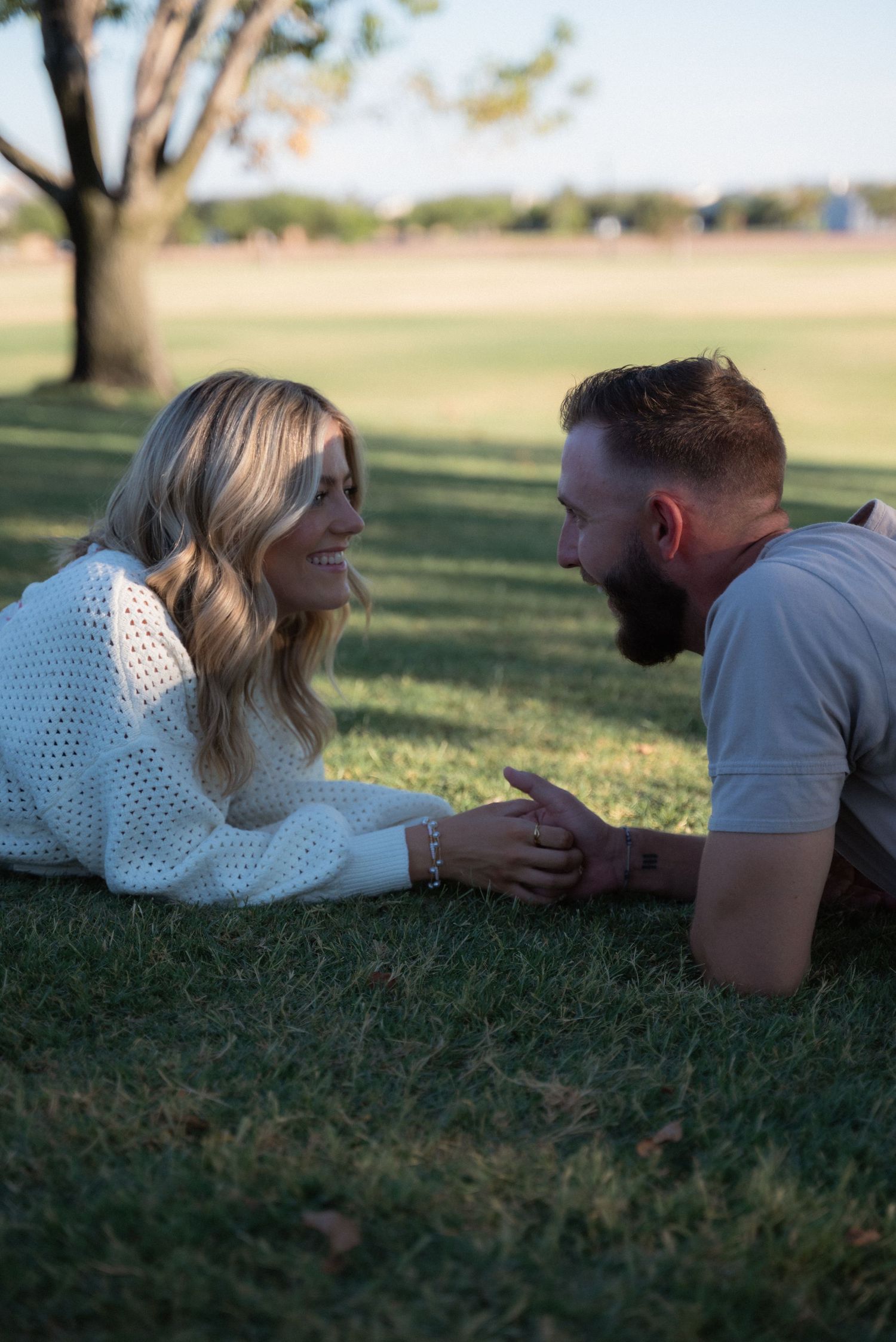 A couple relaxes together on green grass in a sunny park setting.