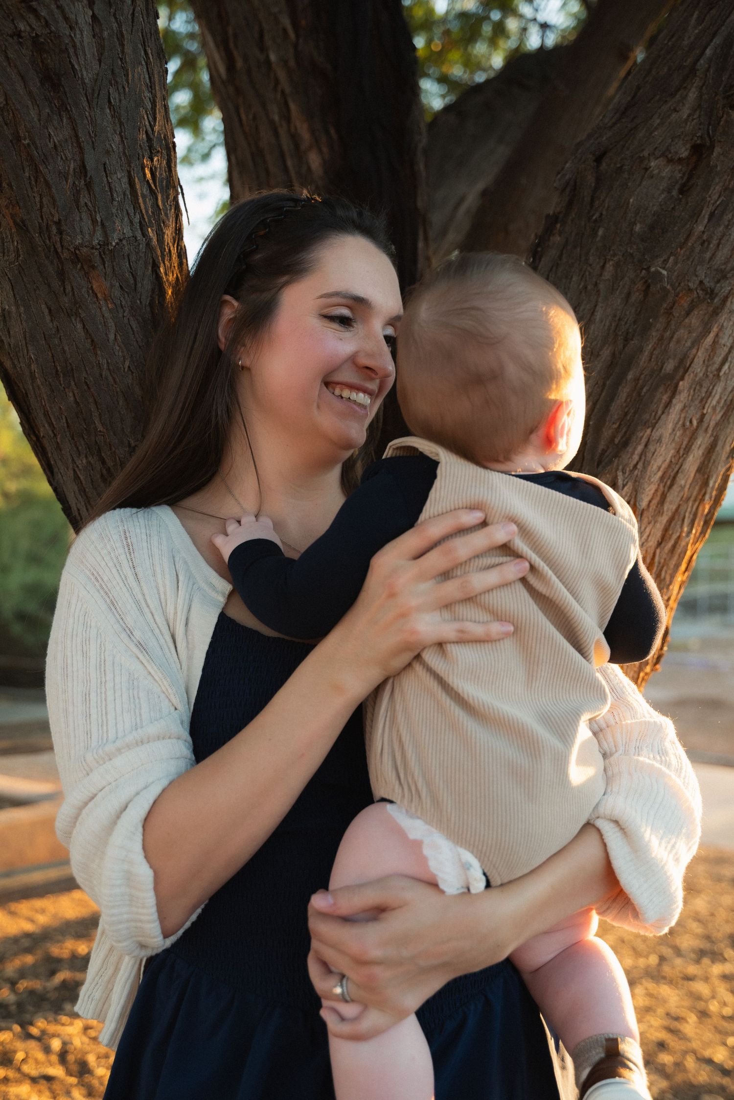 A tender sequence of a parent playfully interacting with their baby in front of a tree during golden hour.