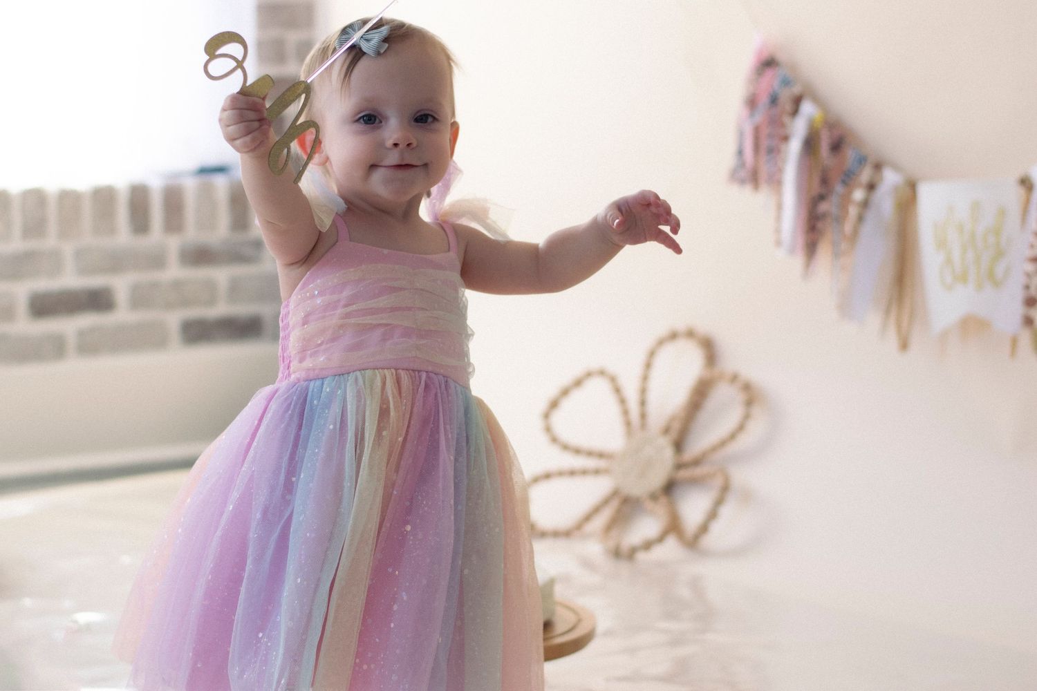 A toddler in a pastel rainbow dress twirls and dances in a room decorated with wall hangings.