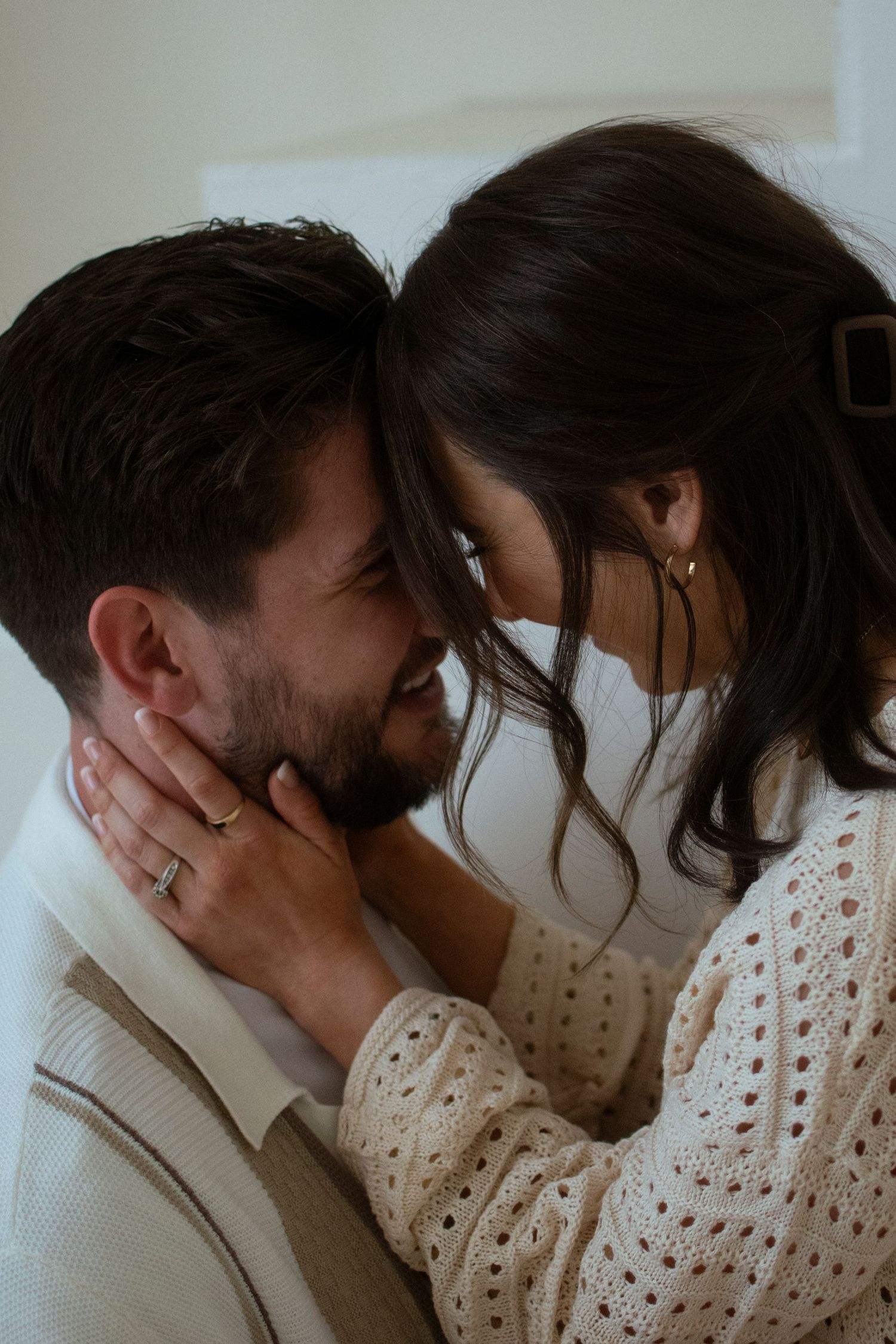 A romantic couple in white sweaters share an intimate moment together, with her hands gently caressing his face.