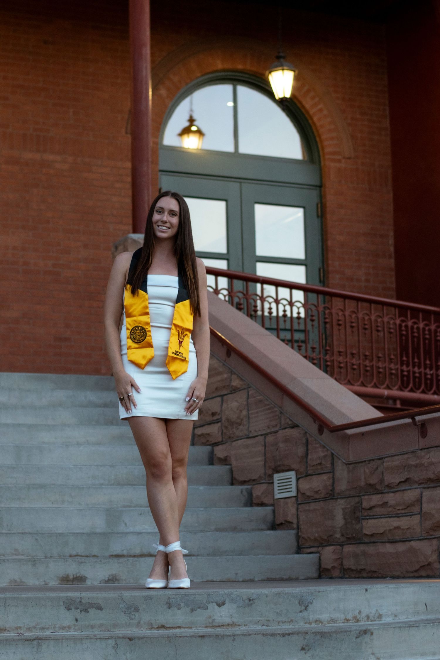 Person wearing a white dress with yellow cartoon character stands on stone steps near brick building.