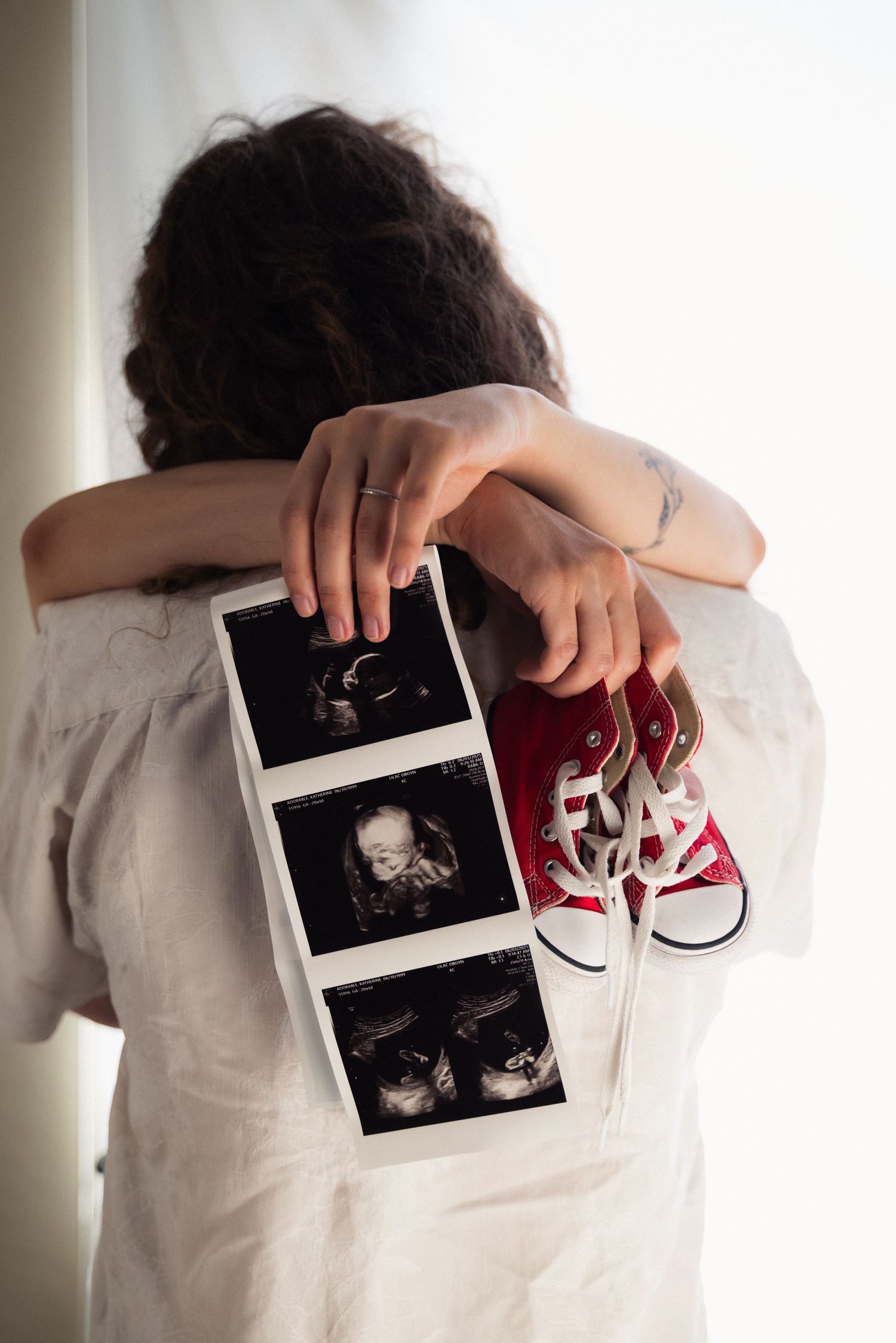 Person in white shirt holding ultrasound photos and baby shoes in progression of reveal images.