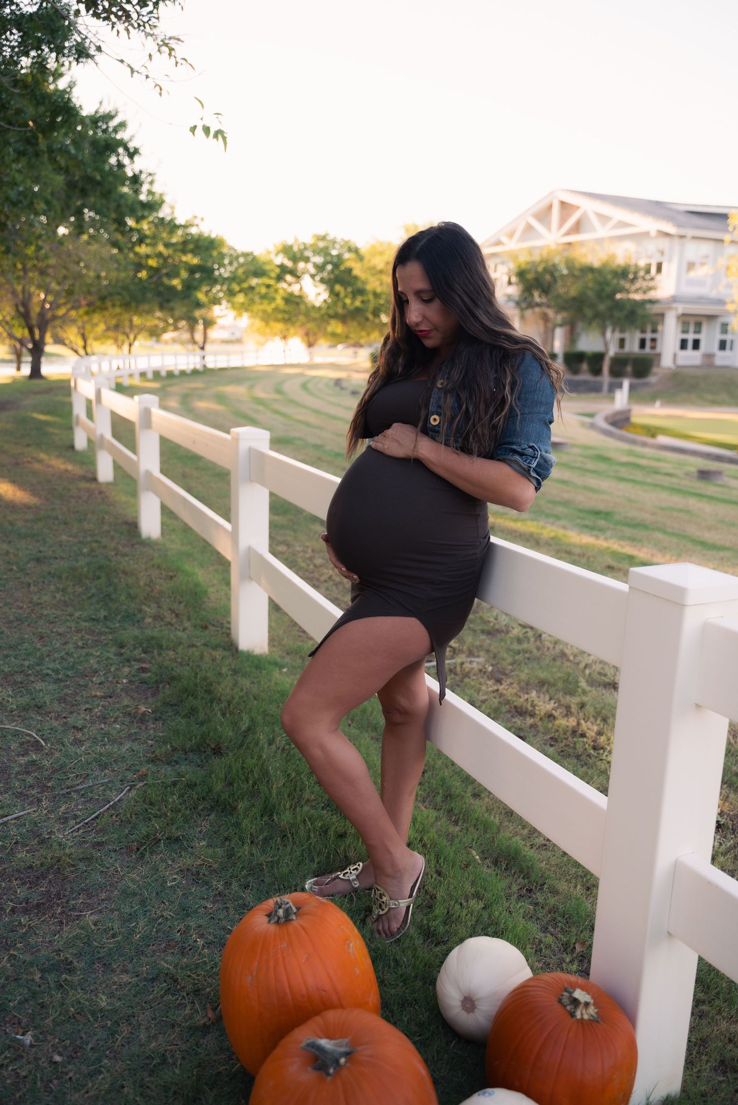 A person poses with pumpkins along a white fence at sunset creating a playful autumn scene.