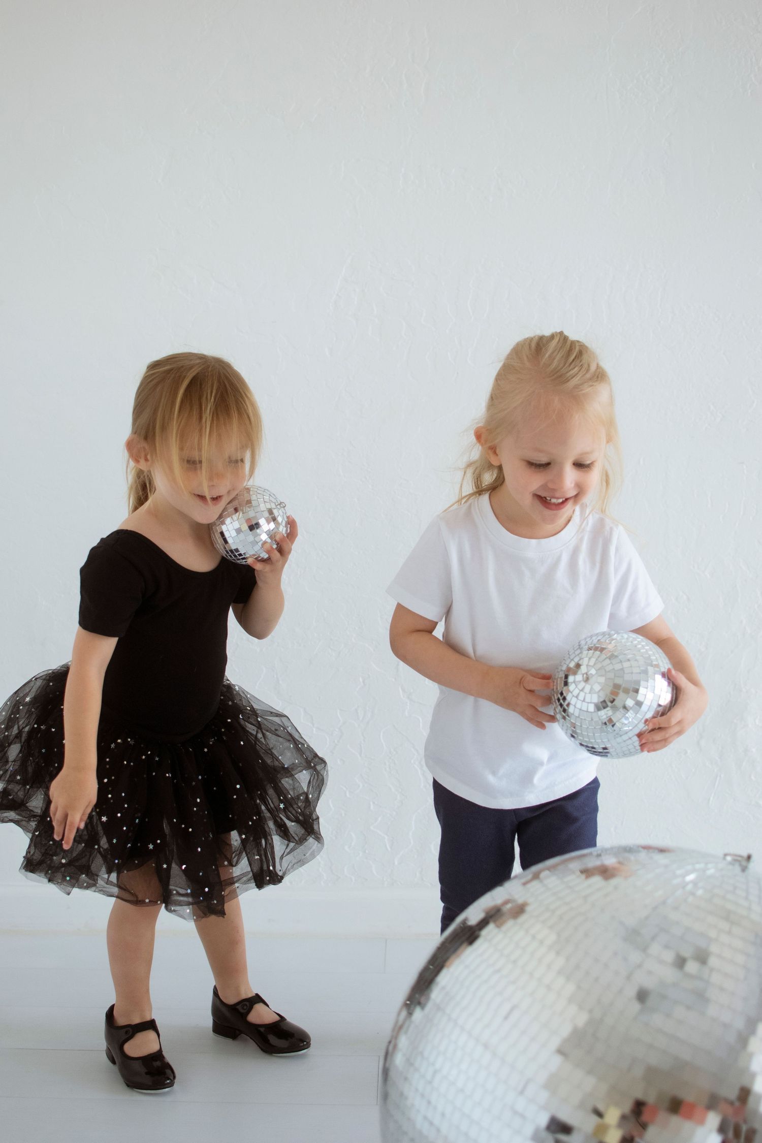 Two children play with disco balls in a bright white studio setting.