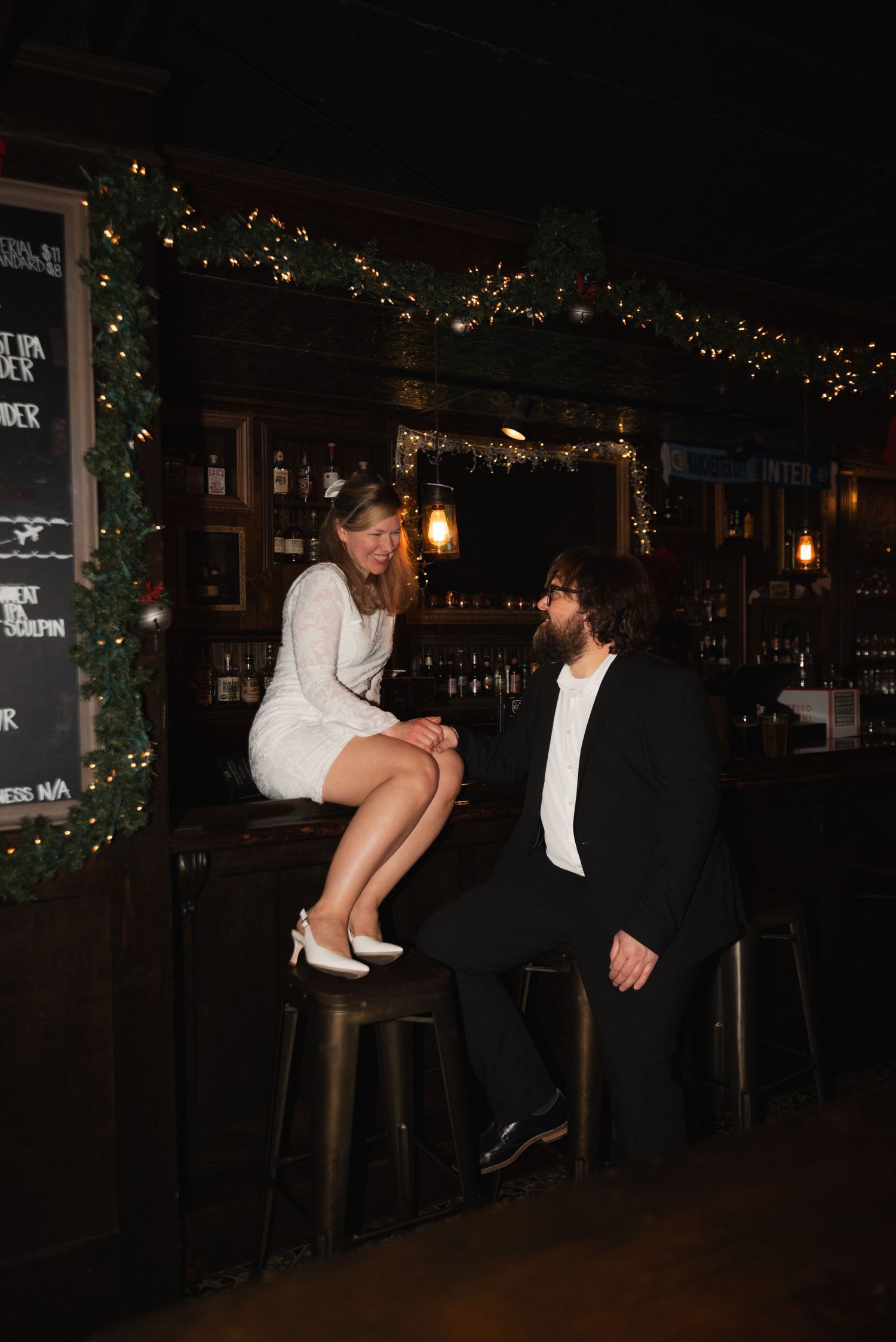 A couple in formal attire share a romantic dance moment in a dimly lit bar with twinkling lights in the background.
