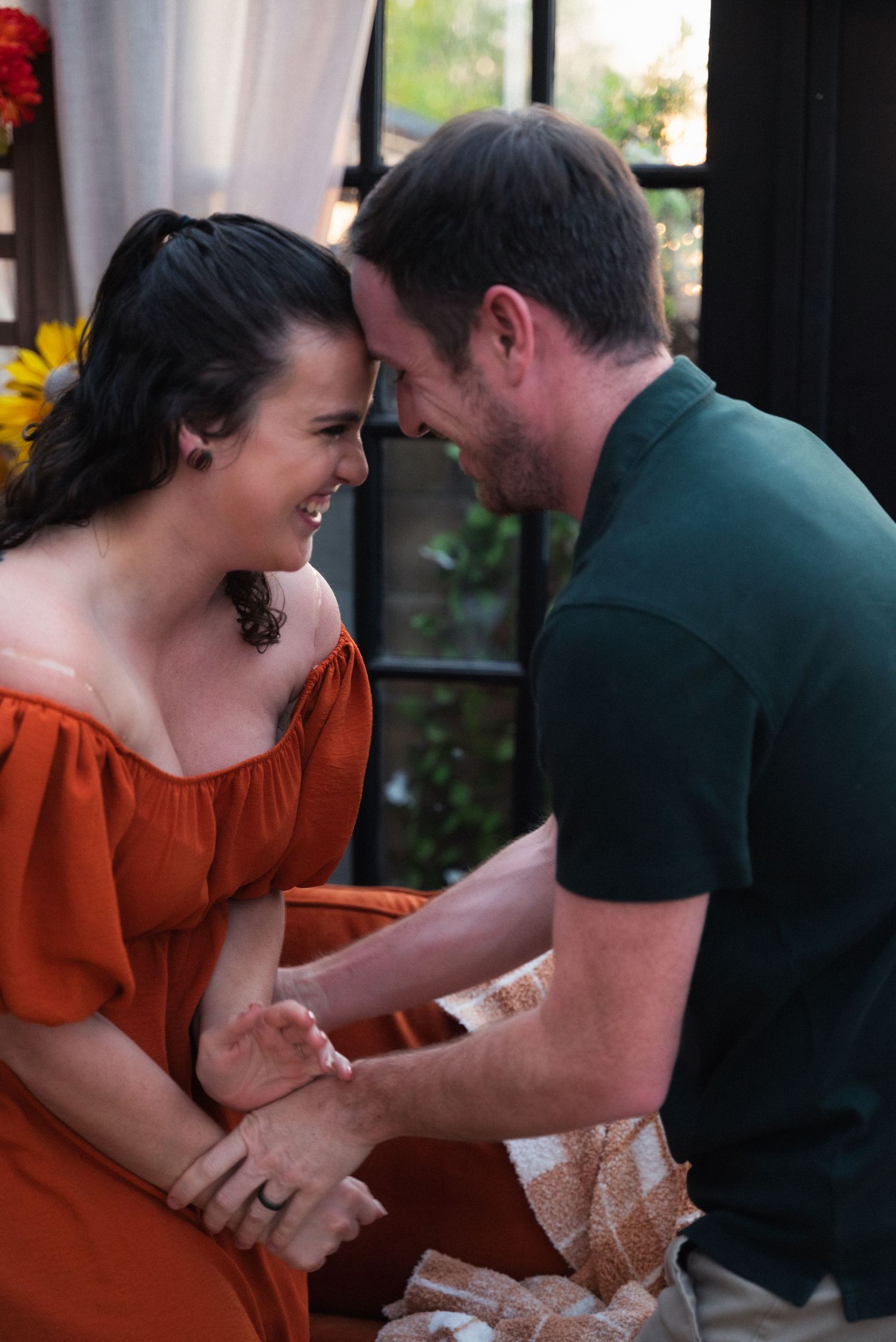A couple in a romantic moment share laughter and tender gestures while sitting together at a table.