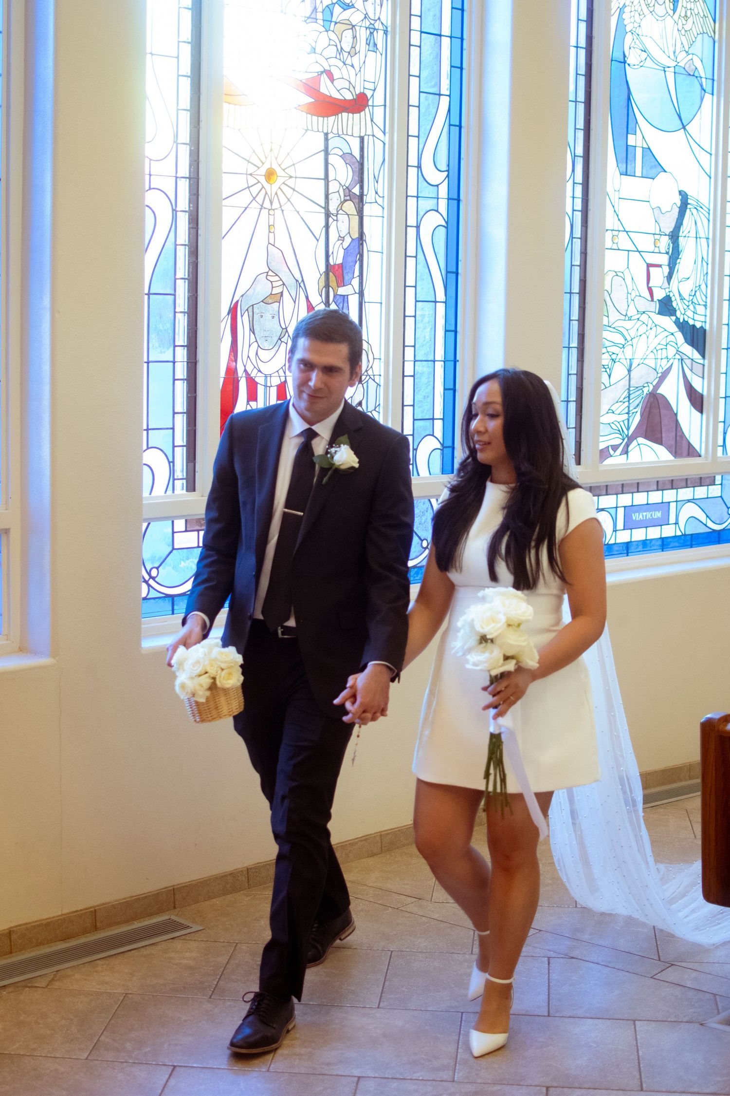 Wedding couple playfully run and dance together in a church hallway with stained glass windows.