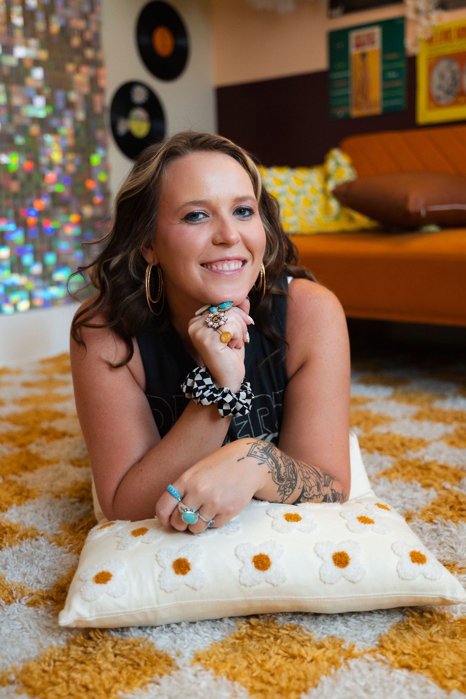 A smiling individual rests on a white pillow with glittery background and record albums visible on wall.