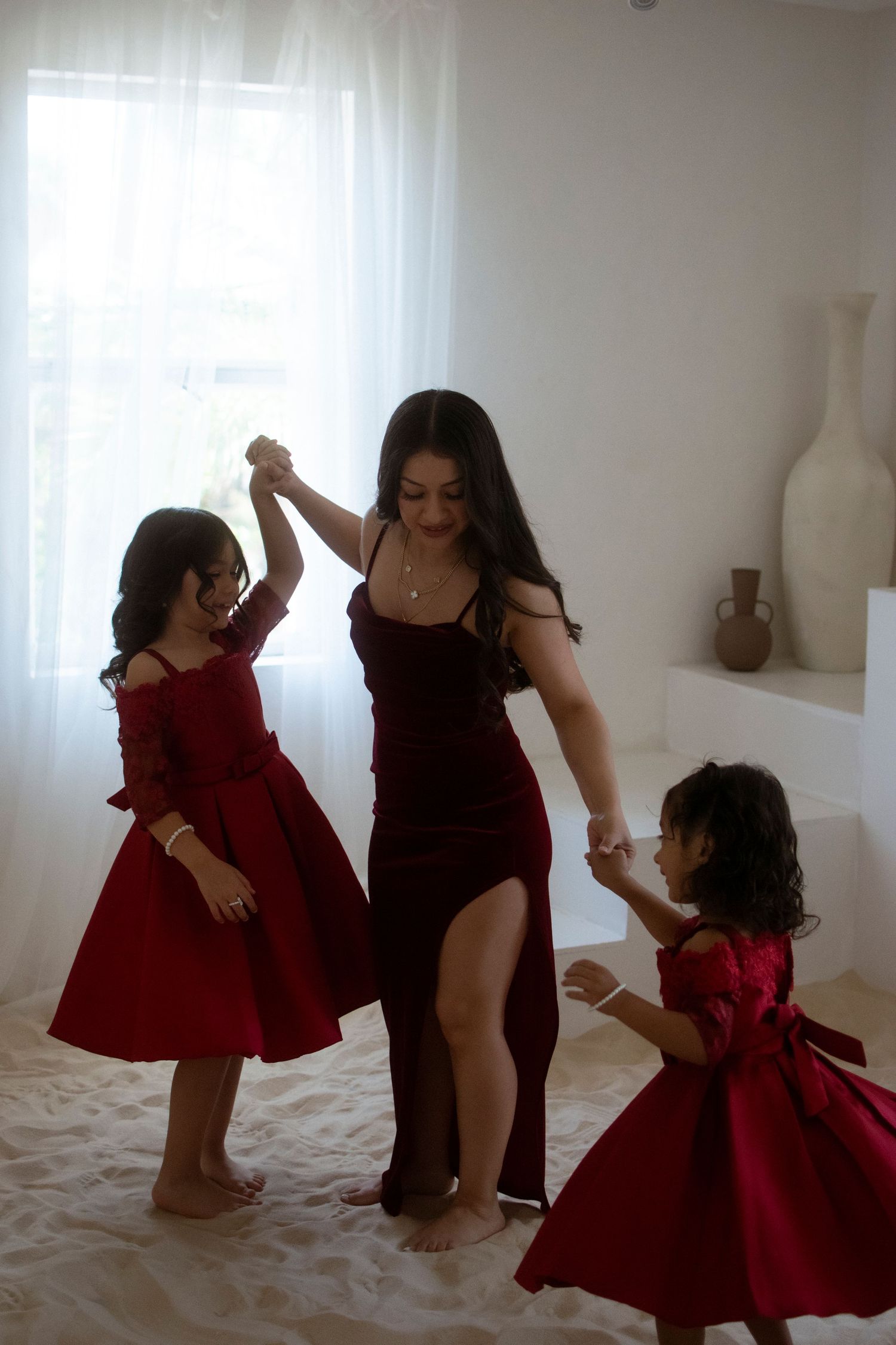 Three people in red dresses dance together in a bright room.