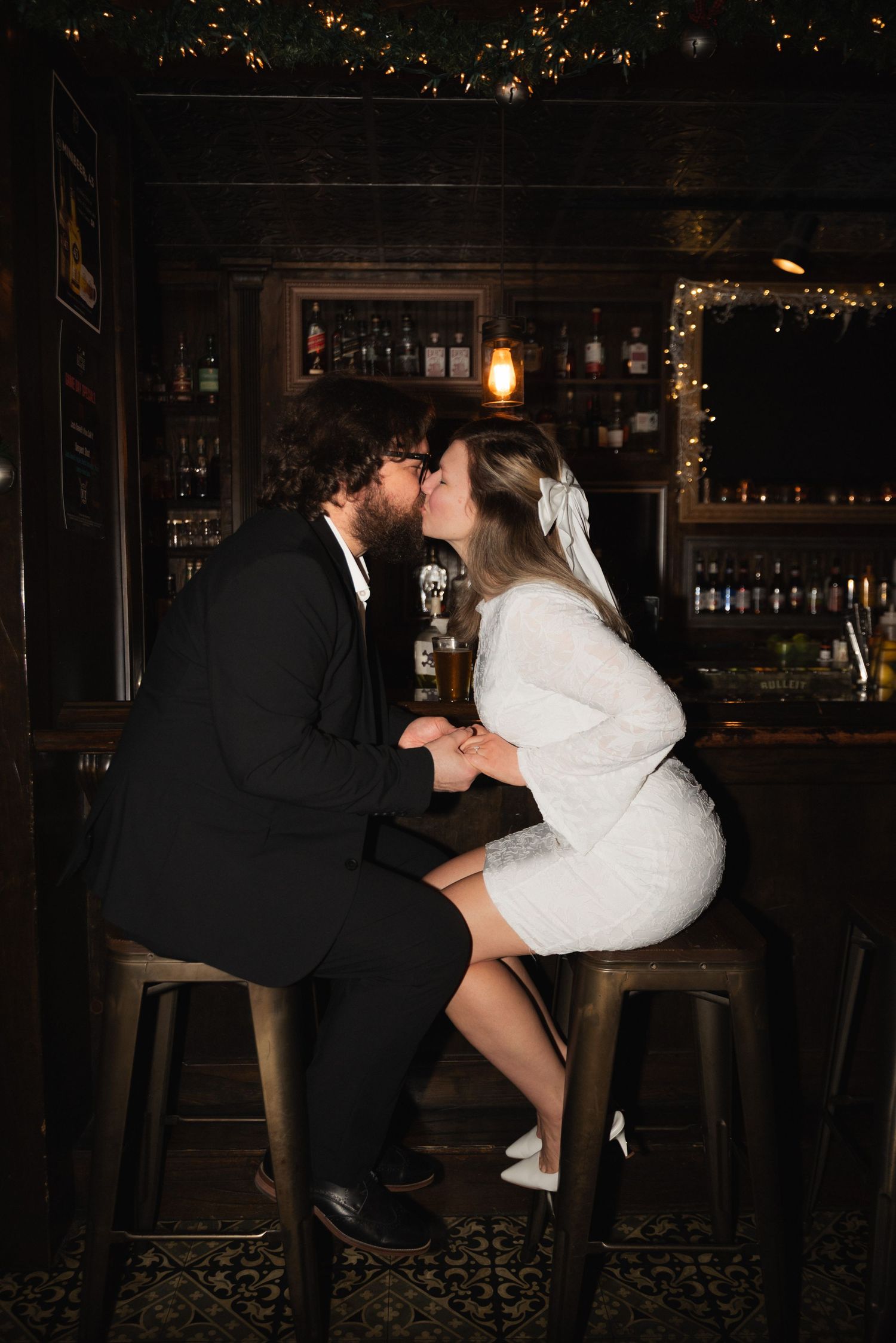 Two people dancing intimately in a dark bar setting with decorative lights and bar stools visible.