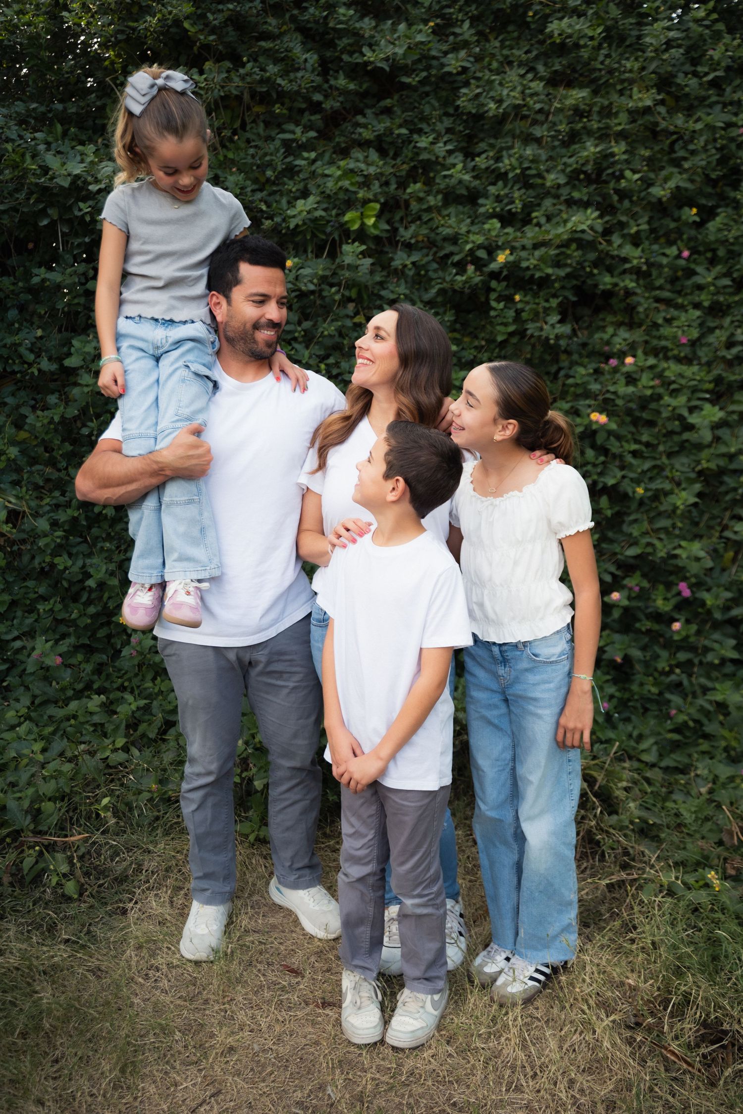 A family wearing coordinated casual outfits poses and laughs together against a green leafy background.