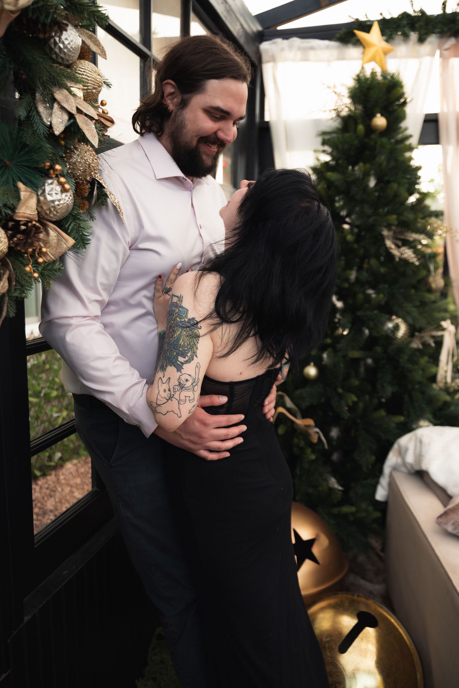 A romantic couple embraces near a decorated Christmas tree with twinkling lights and festive decorations.