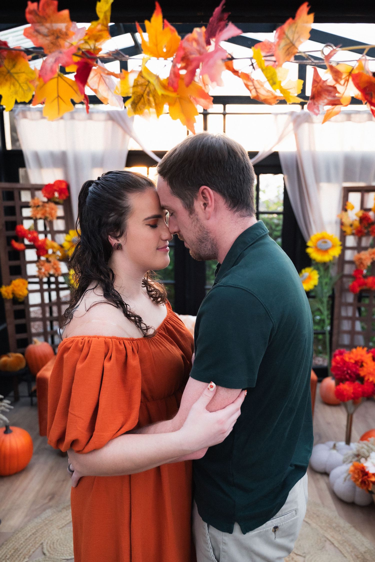 A romantic autumn scene with colorful maple leaves hanging above a couple in orange and green embracing.