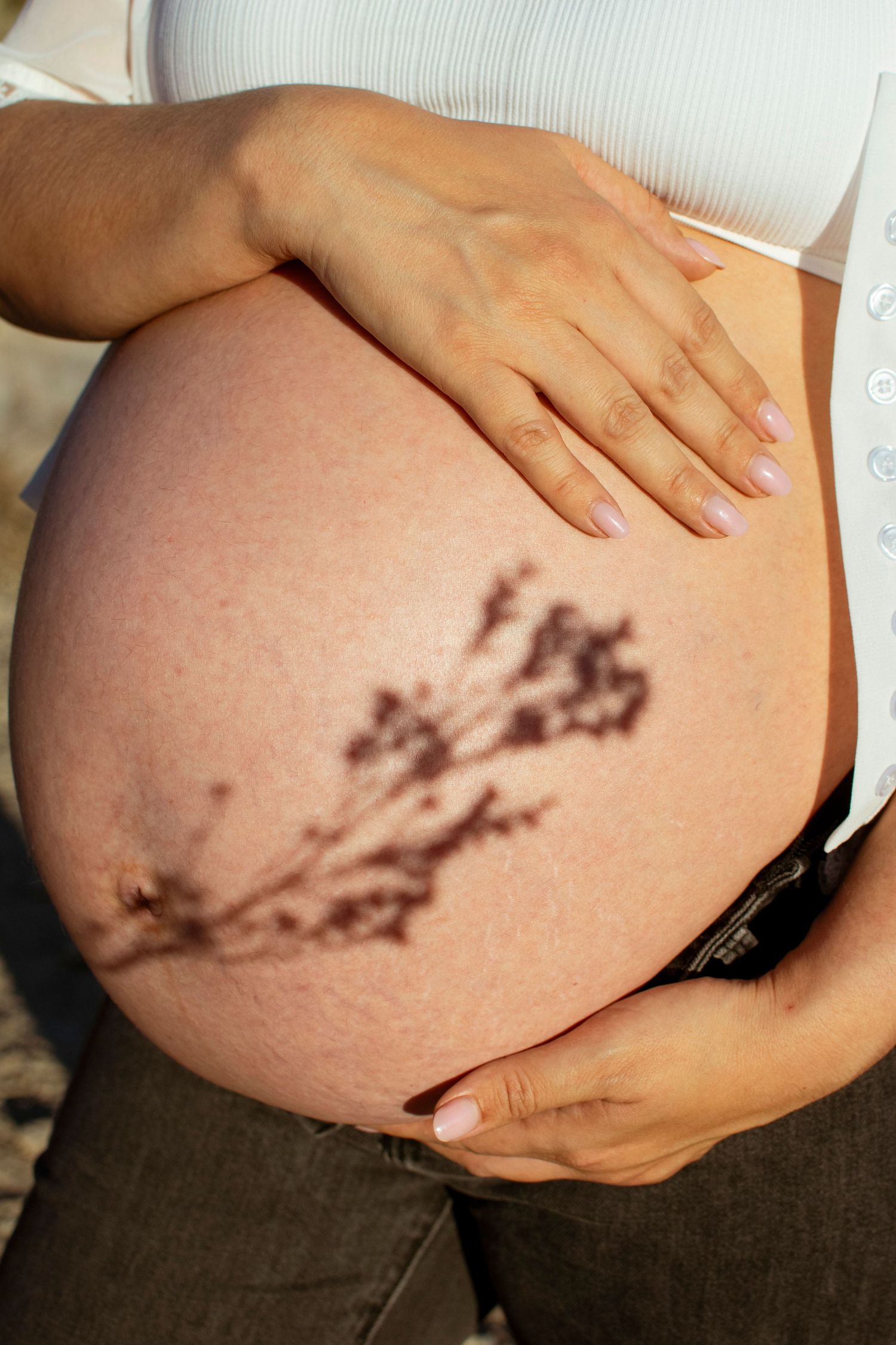 Close-up of hands cradling a pregnant belly with a shadow pattern cast across the skin.