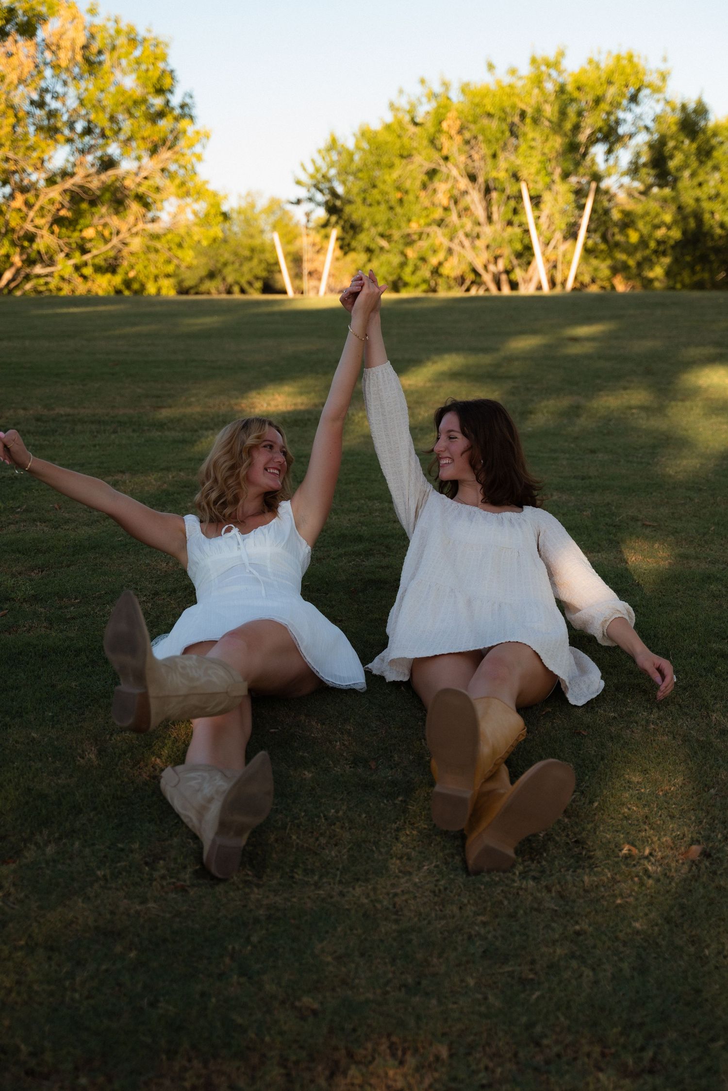 Two people in white outfits lying on grass having fun together during golden hour sunset.