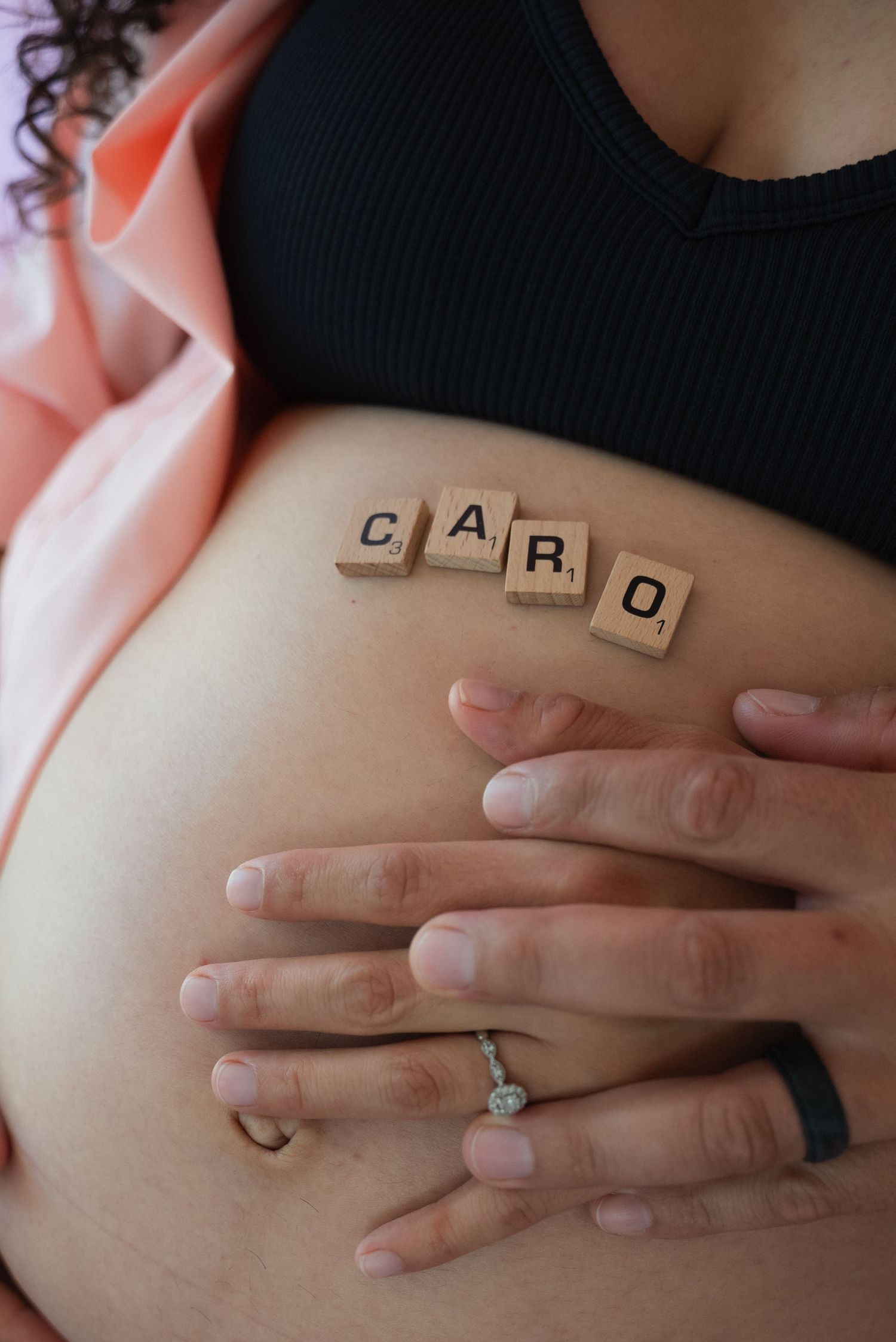 A sequence of hands holding wooden letter blocks spelling out a word against a soft pink background.