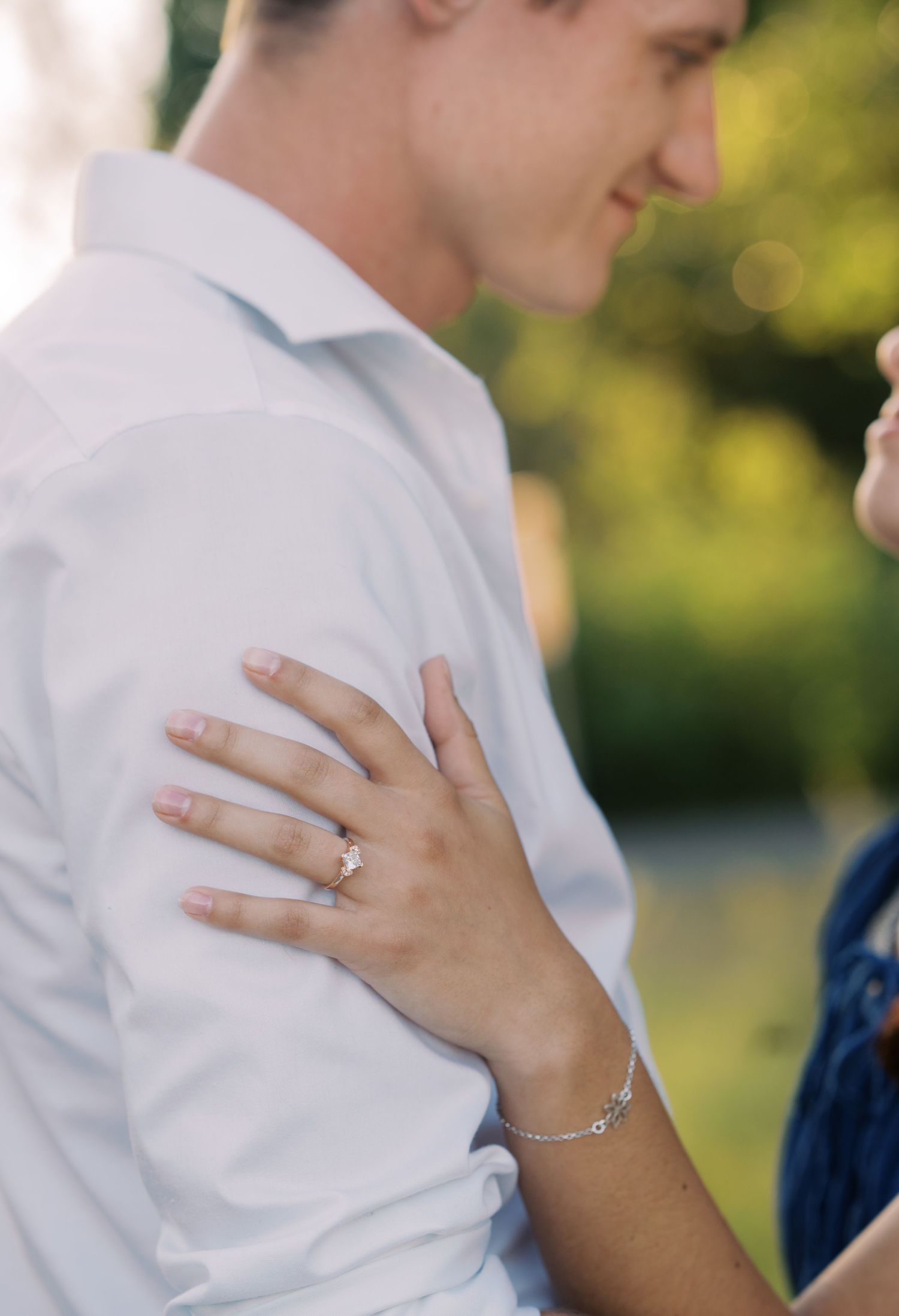 Close-up of a woman resting her hand on a mans shoulder showing an engagement ring and bracelet.