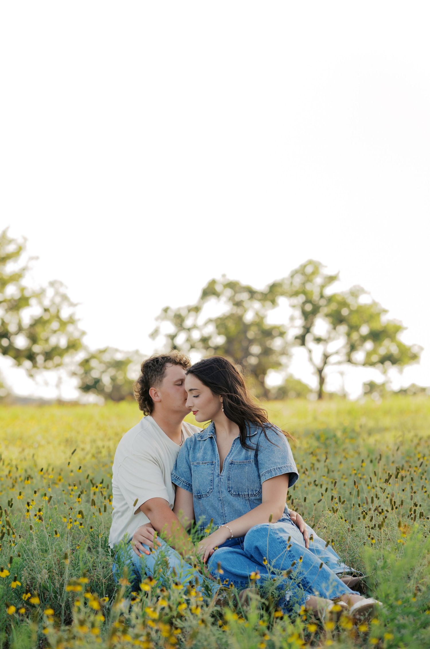 Couple sharing a tender kiss while sitting together in a vibrant yellow wildflower meadow.