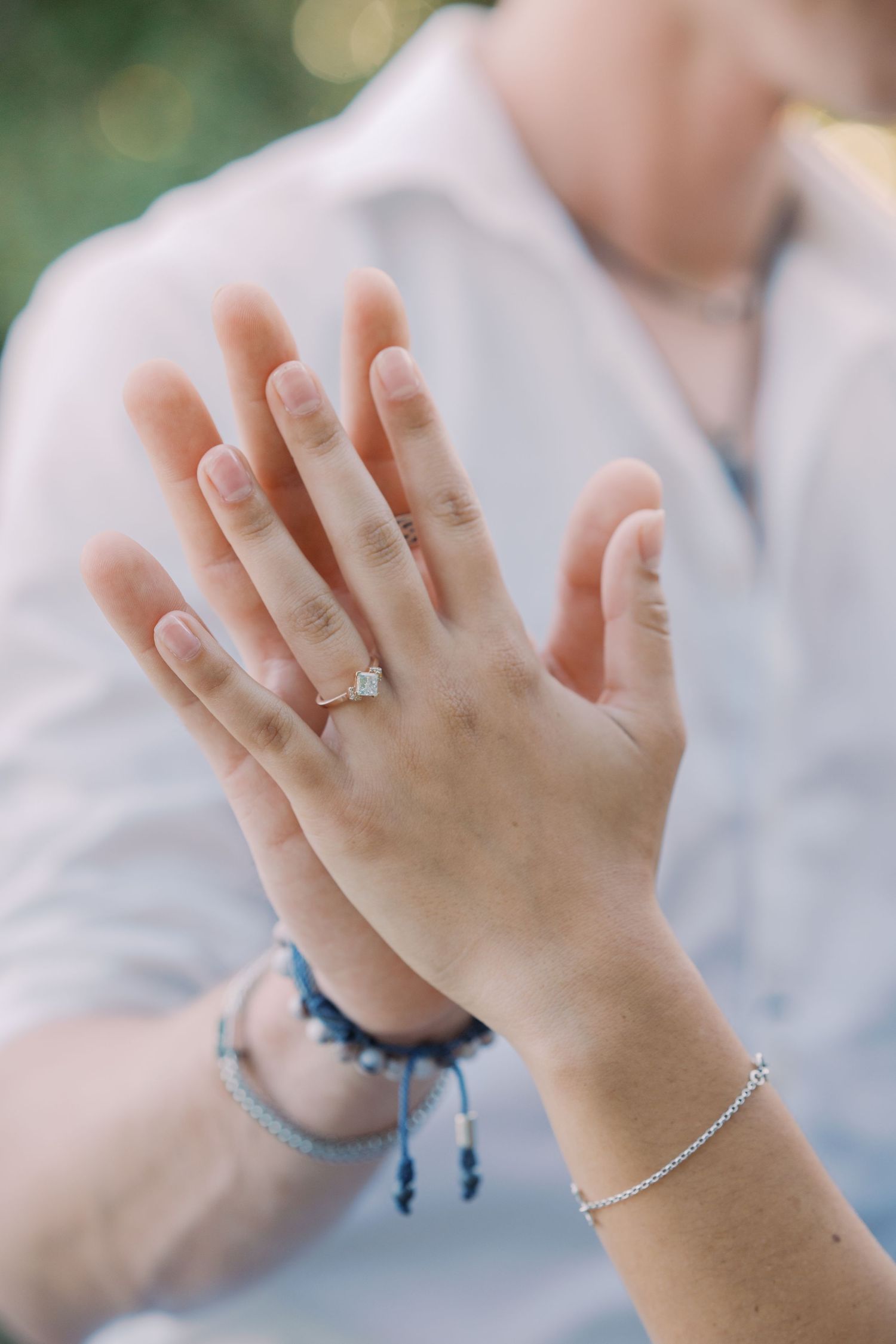 Close-up of two hands touching, woman wearing diamond engagement ring and silver bracelet, man in blue shirt.